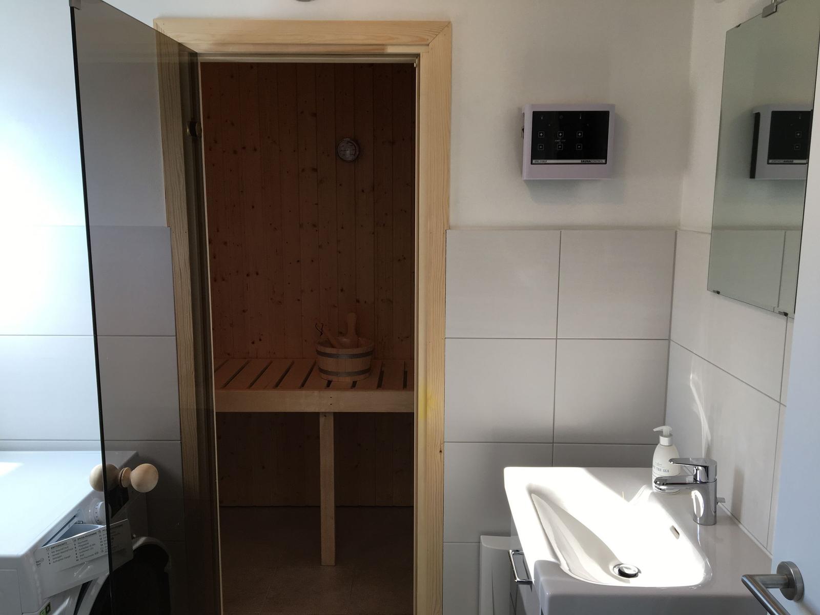Sauna mit Holzbank und Korb, daneben Waschbecken und Spiegel.