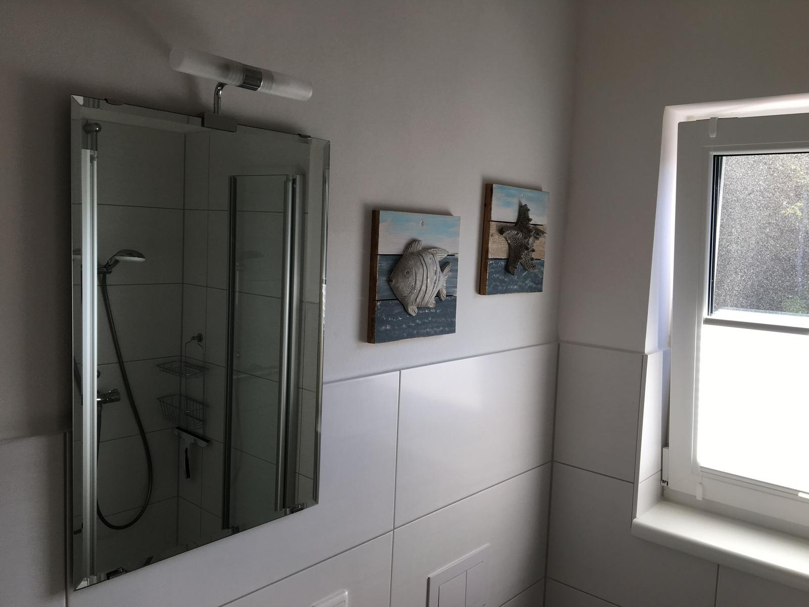 Badezimmer mit Dusche, Spiegel und Fenster. Wanddekoration mit Fisch und Seestern.