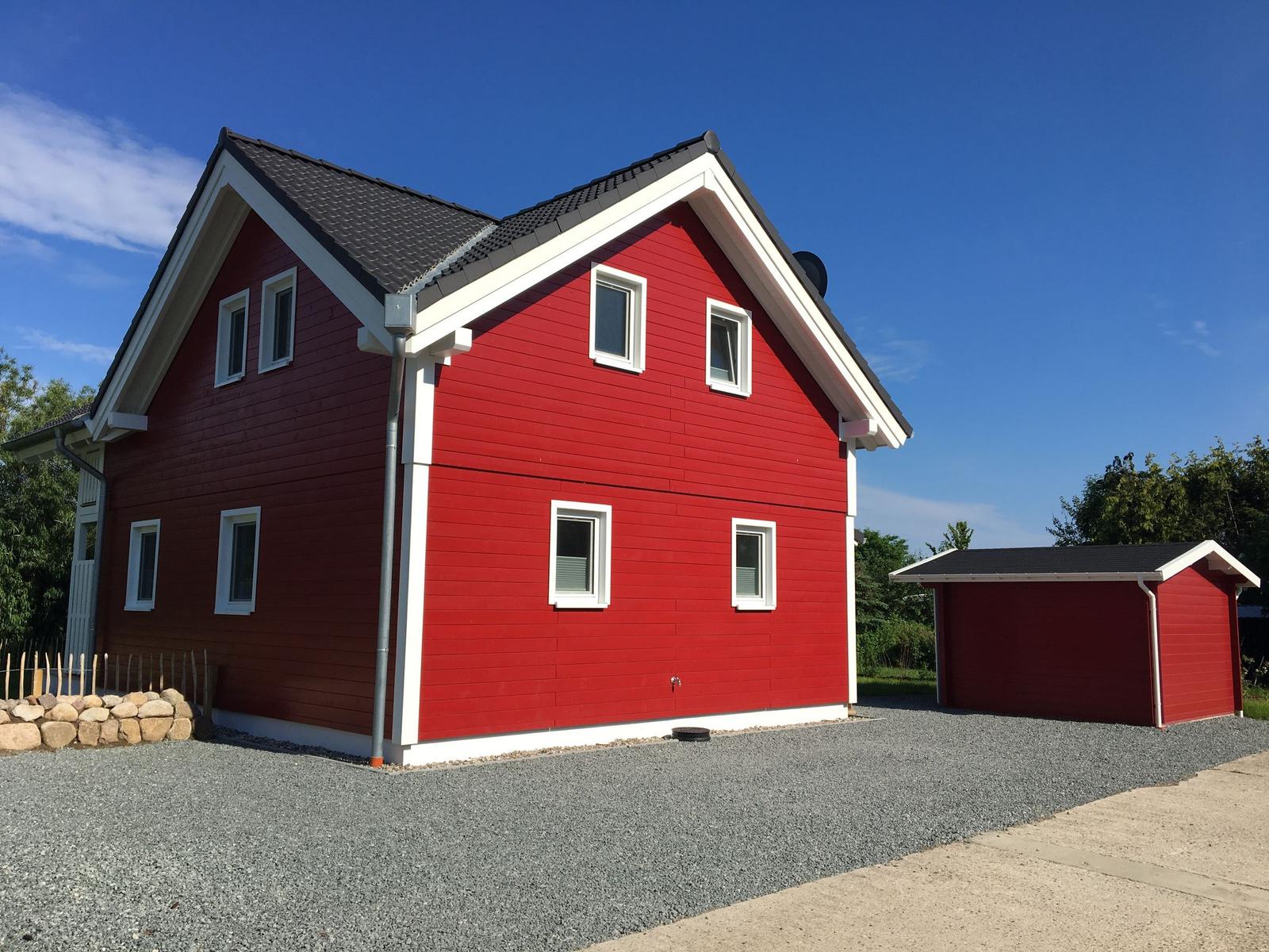 Rotes Haus mit weißen Fensterrahmen und Garage. Gravierter Boden und blauer Himmel.