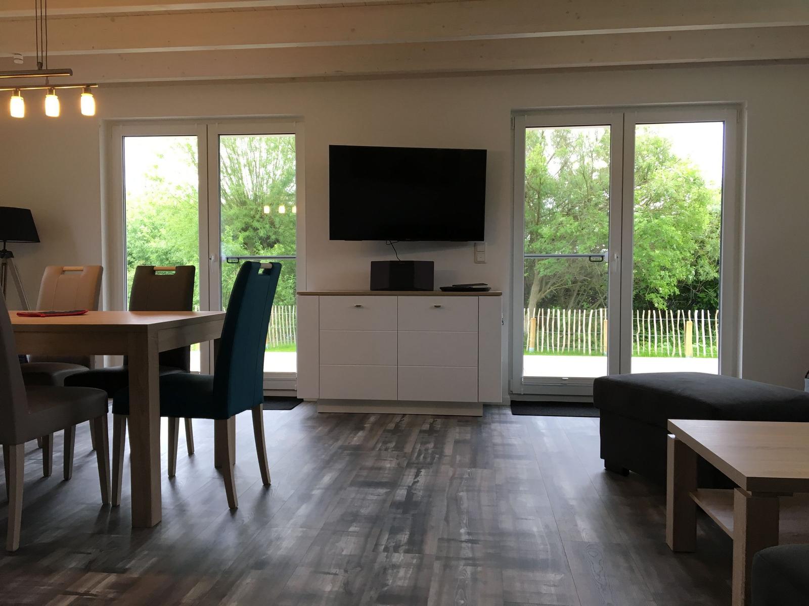 Wohn- und Essbereich mit TV, Balkon und Holzboden.