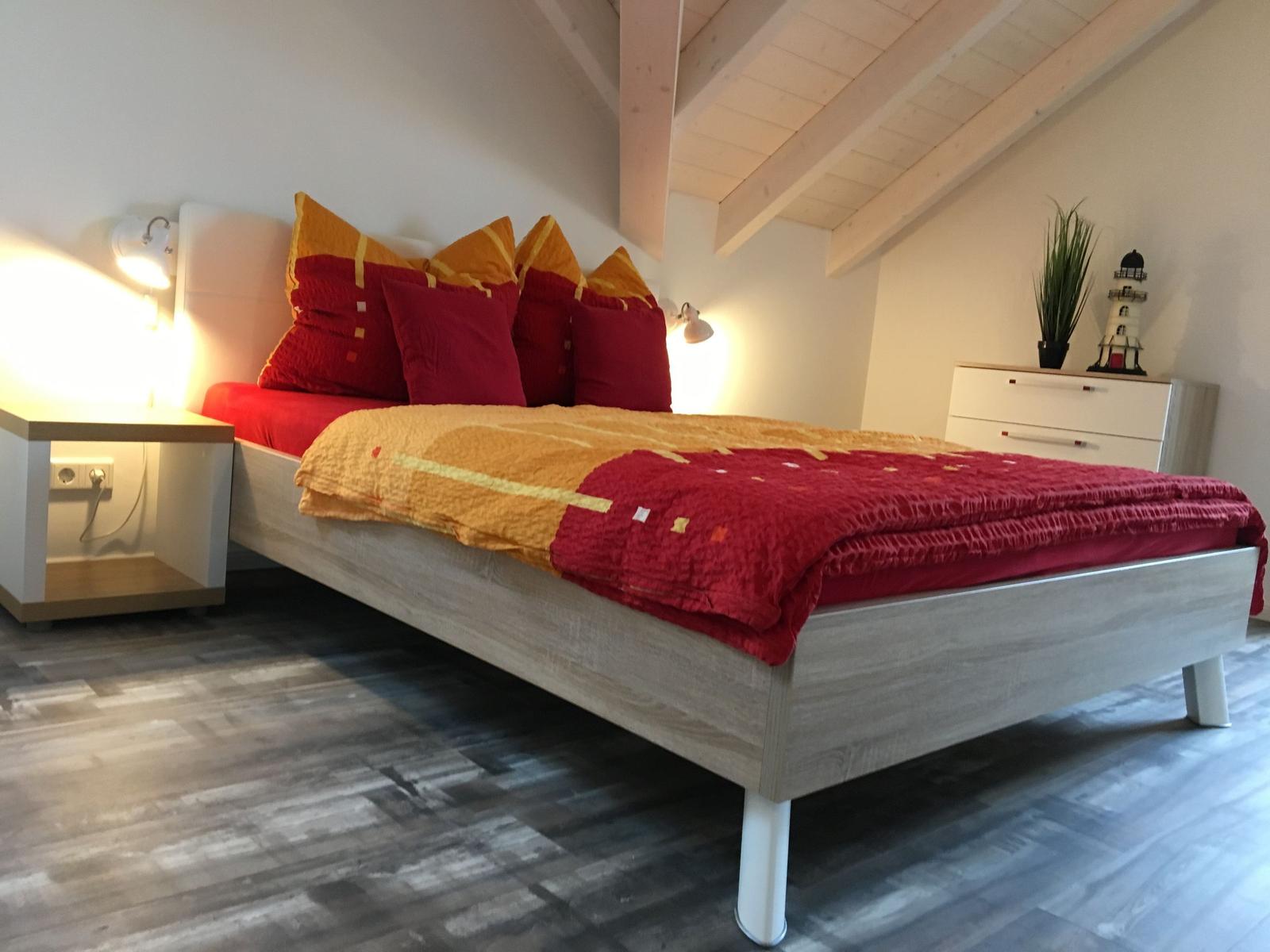 Schlafzimmer mit Bett, Nachttisch und Schrank unter Holzbalkendecke.