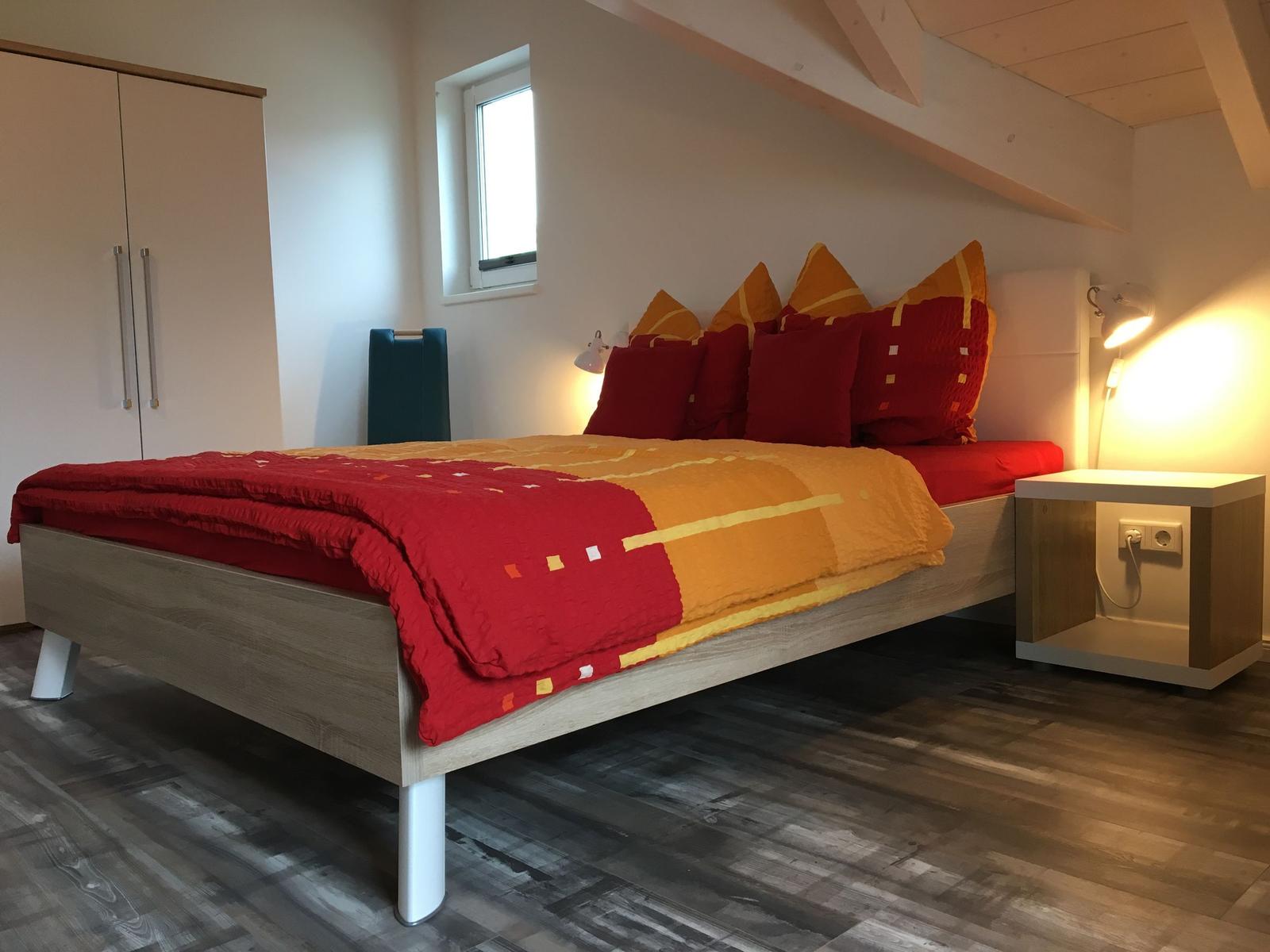 Schlafzimmer mit Bett, Nachttisch und Kleiderschrank unter Dachschrägen.