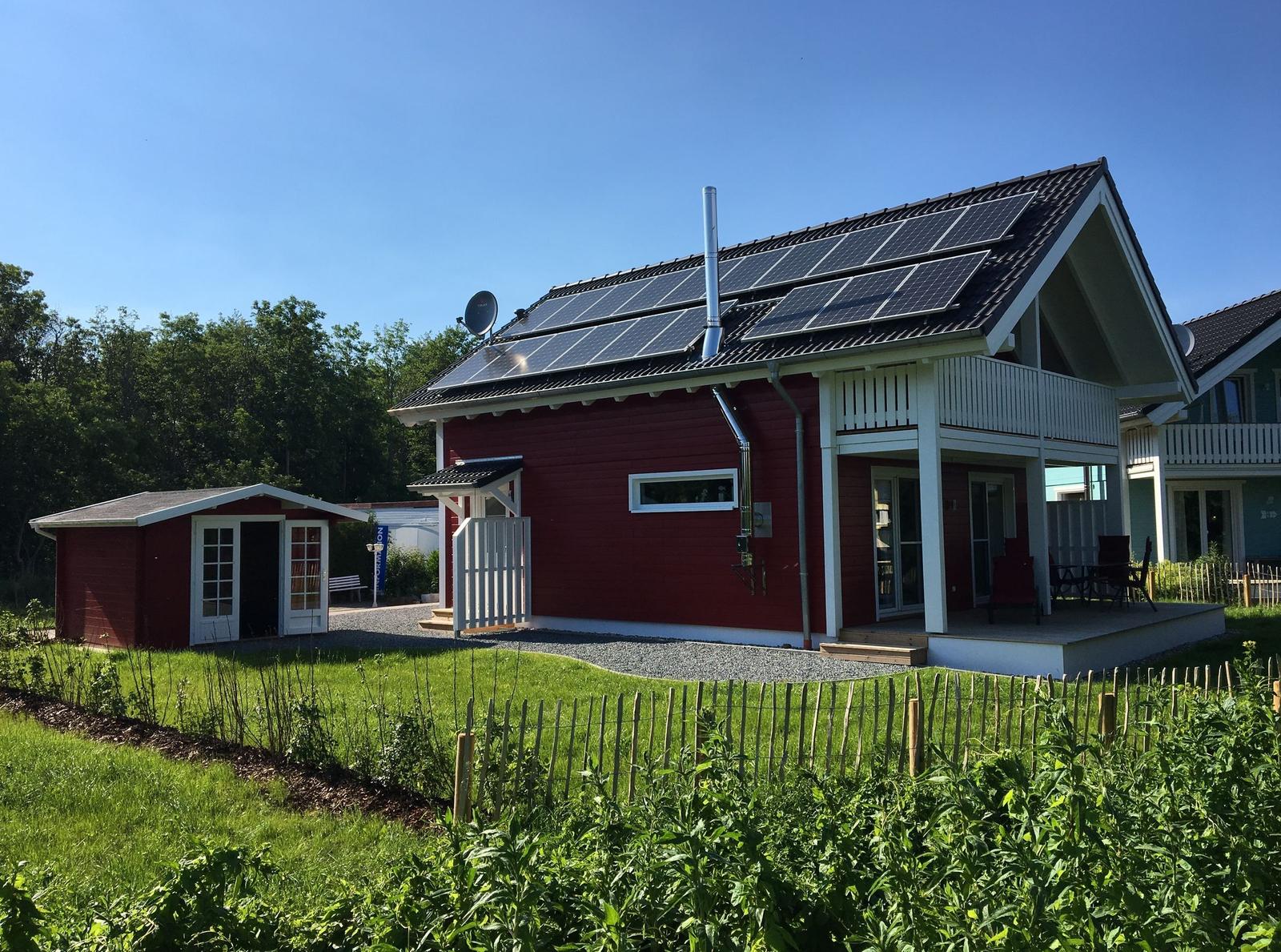 Rotes Haus mit Solaranlage und Balkon. Nebenhaus und Garten sind sichtbar.