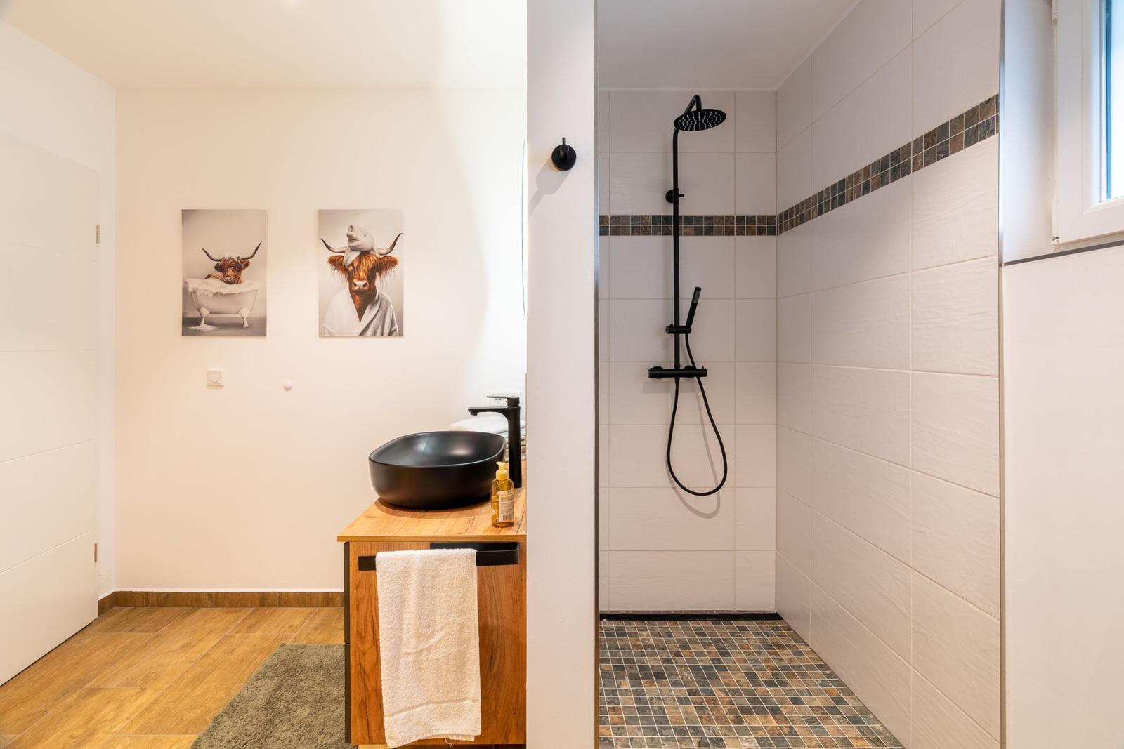 Bad mit Dusche, Waschbecken und Wandbildern von Highland-Rindern.