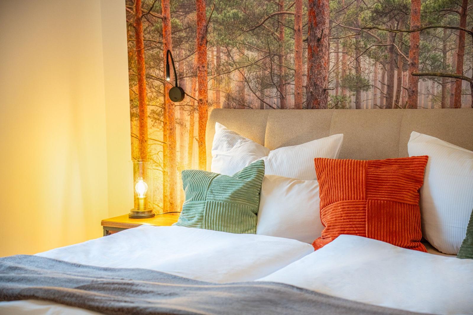 Schlafzimmer mit Bett, Kissen und Waldtapete an der Wand.