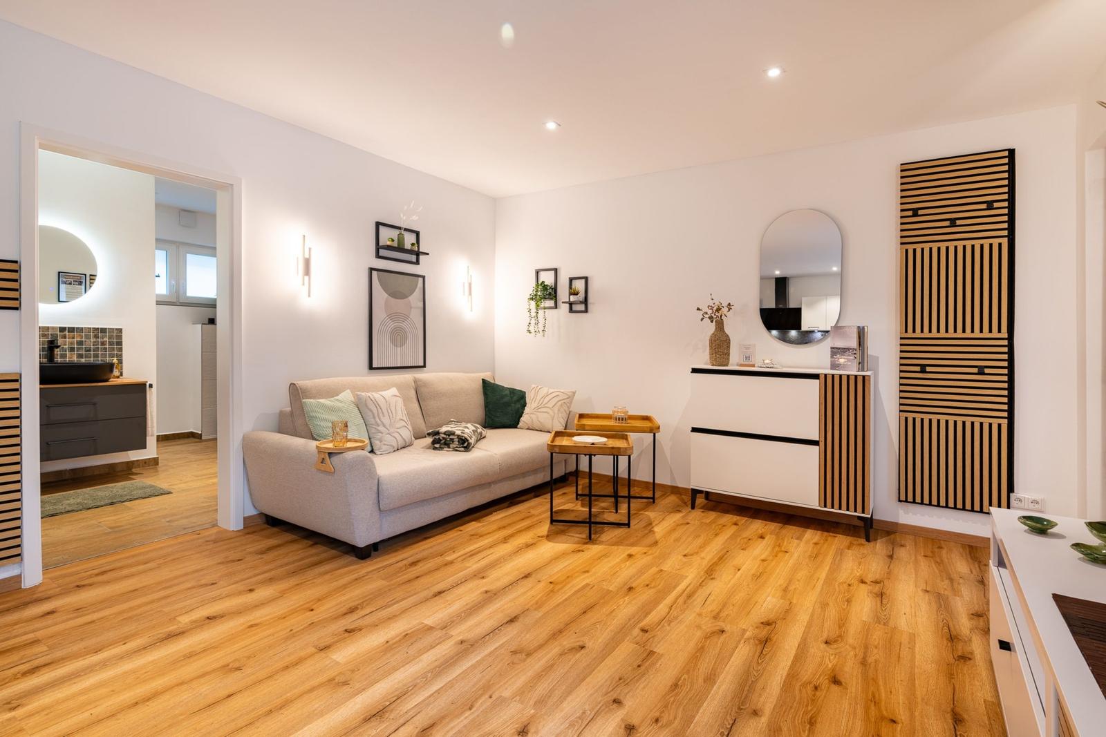 Wohnzimmer mit Sofa, Holzboden und Blick in die Küche