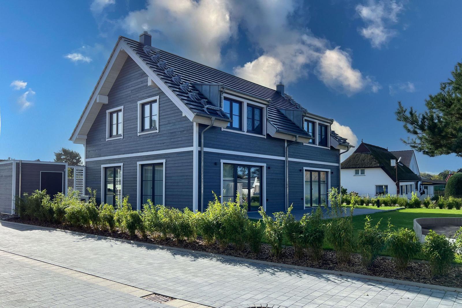 Modernes Haus mit blauer Fassade und weißem Rahmen. Grünflächen und gepflasterte Straße.
