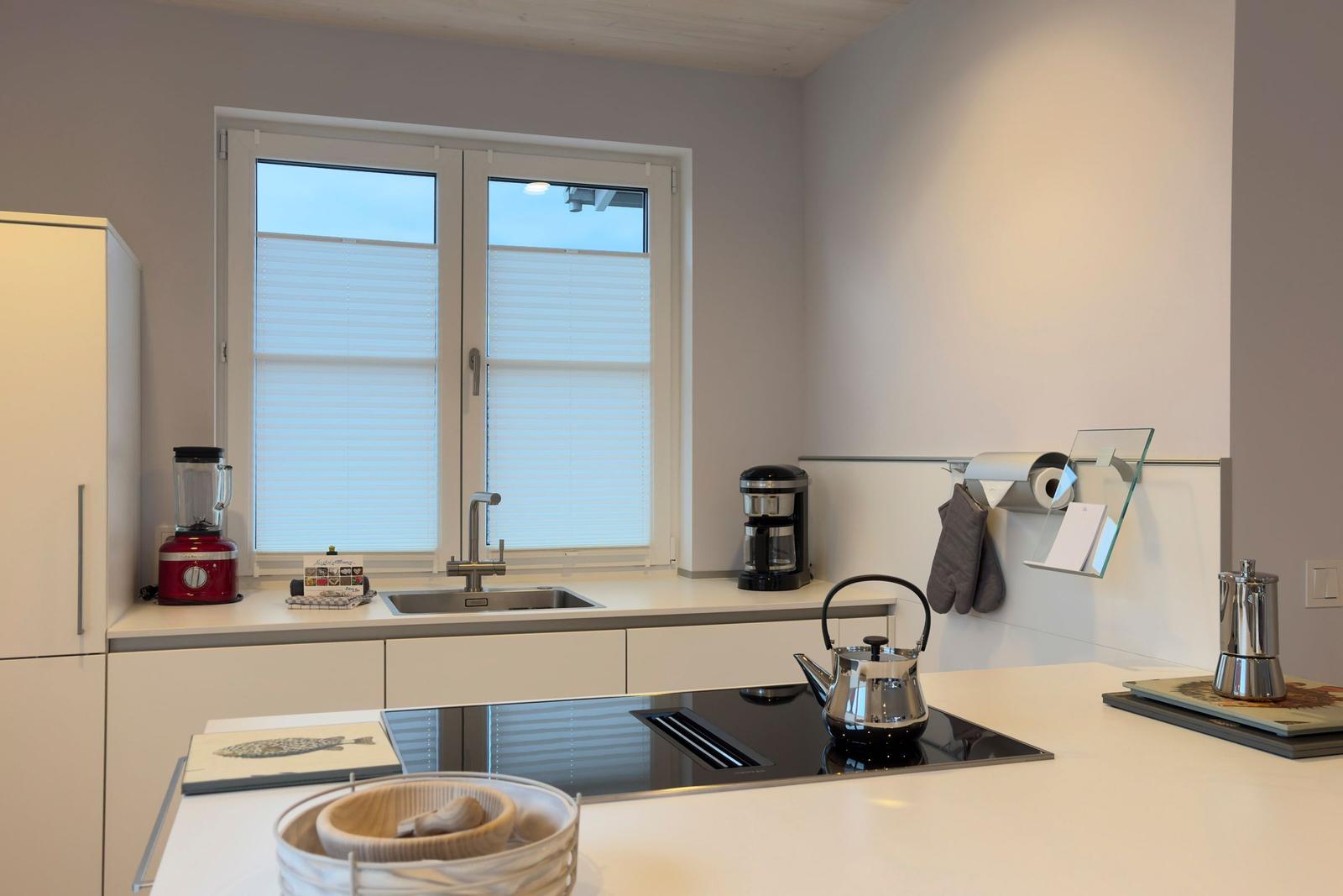Küche mit Arbeitsplatte, Spüle und Fenster mit Jalousien.