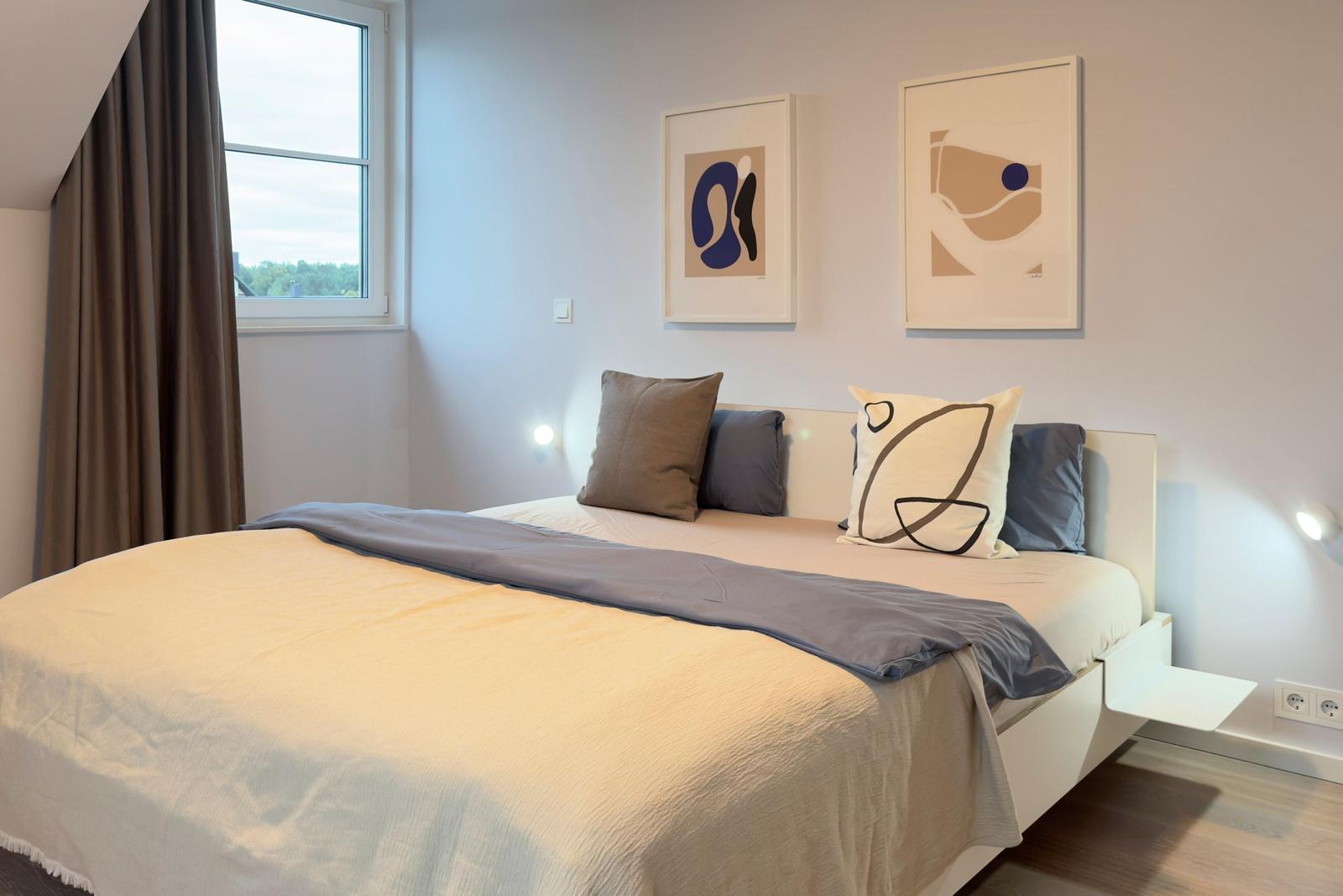 Schlafzimmer mit Bett, Fenster und Wandbildern.