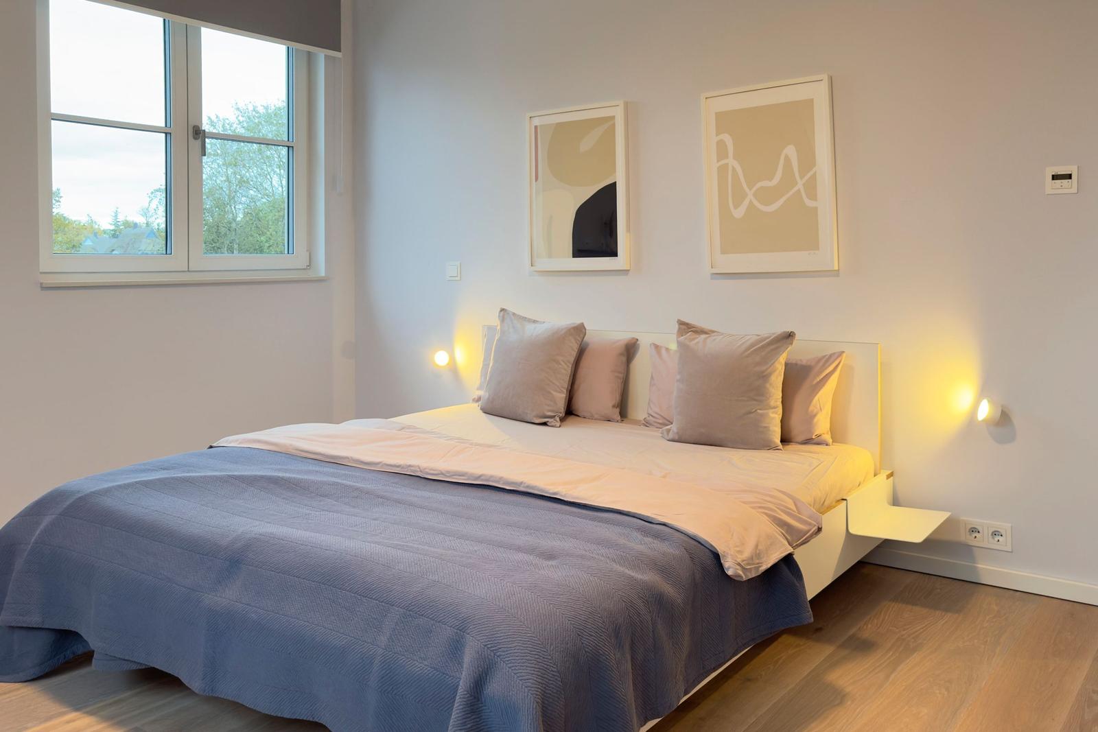 Schlafzimmer mit Bett, Fenster und Wandbildern.