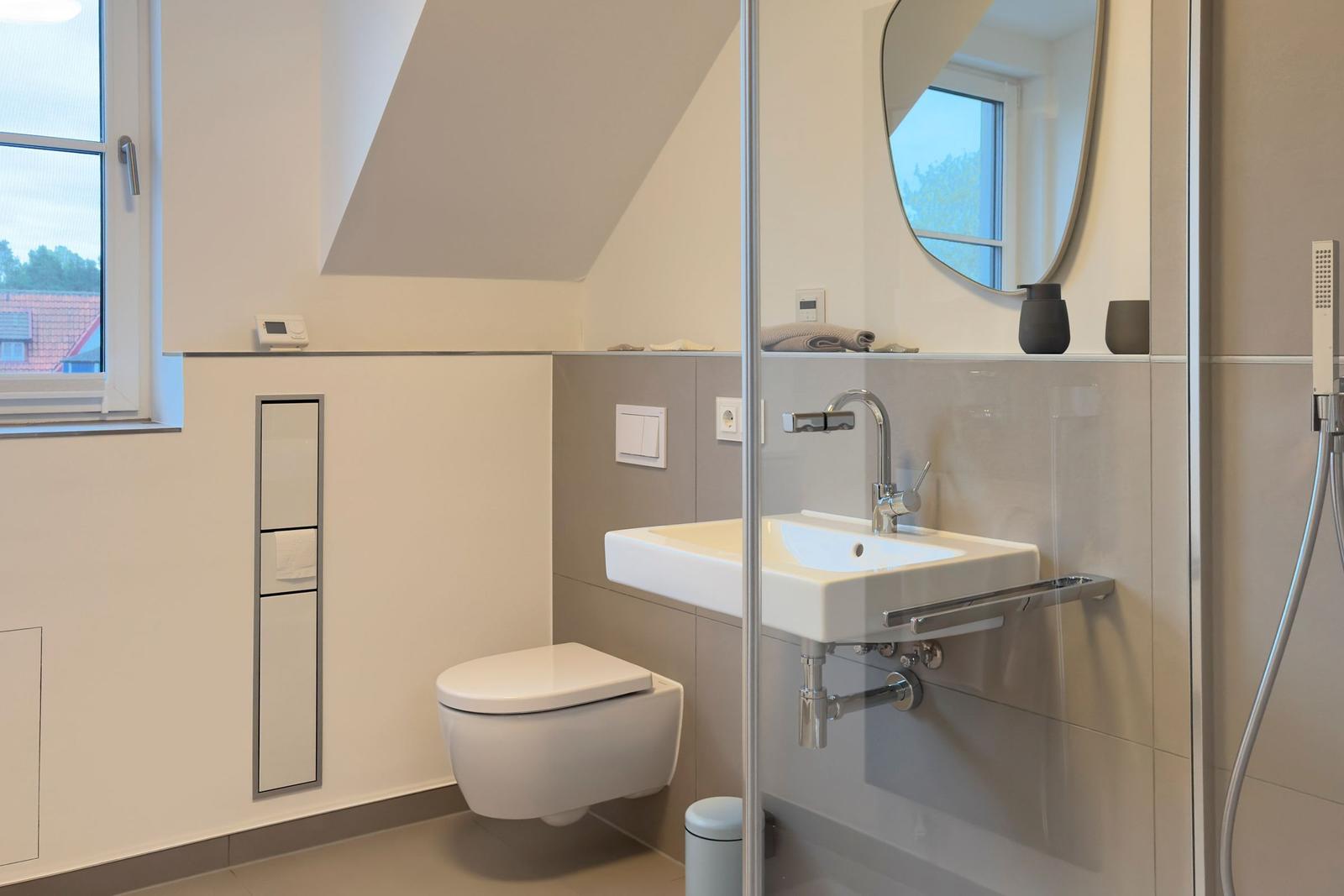 Badezimmer mit Dusche, Waschbecken und Toilette unter Dachschrägen.
