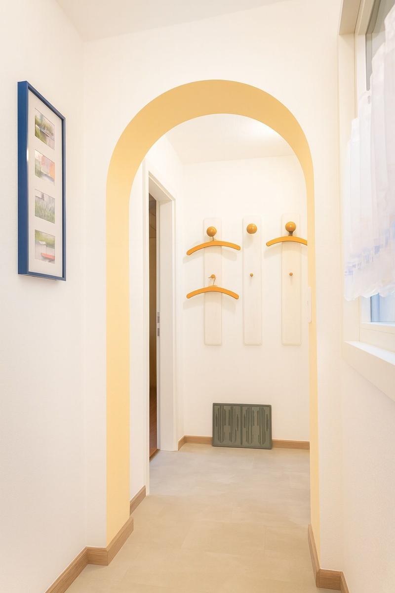 Flur mit gelbem Bogen, Garderobe und Fenster mit Vorhang
