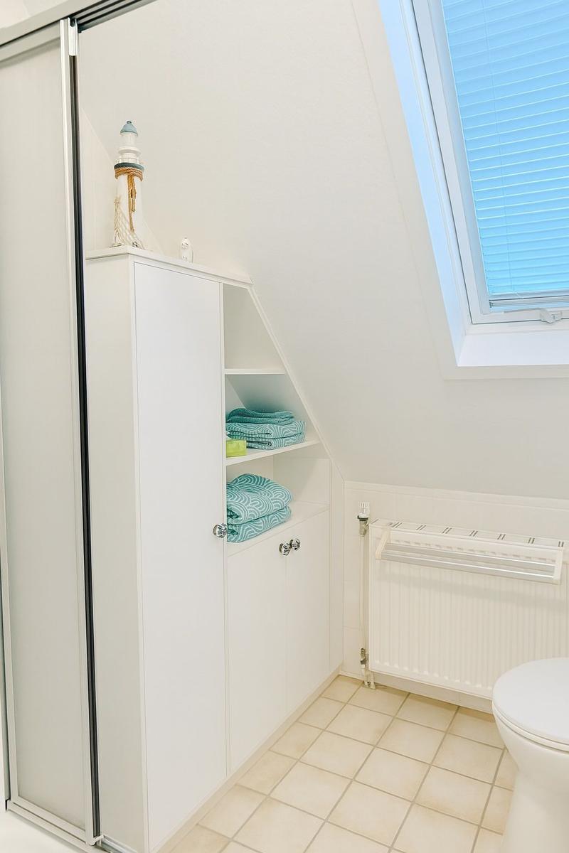 Badezimmer mit Dachschrägen, Schrank, Duschabtrennung und Toilette.