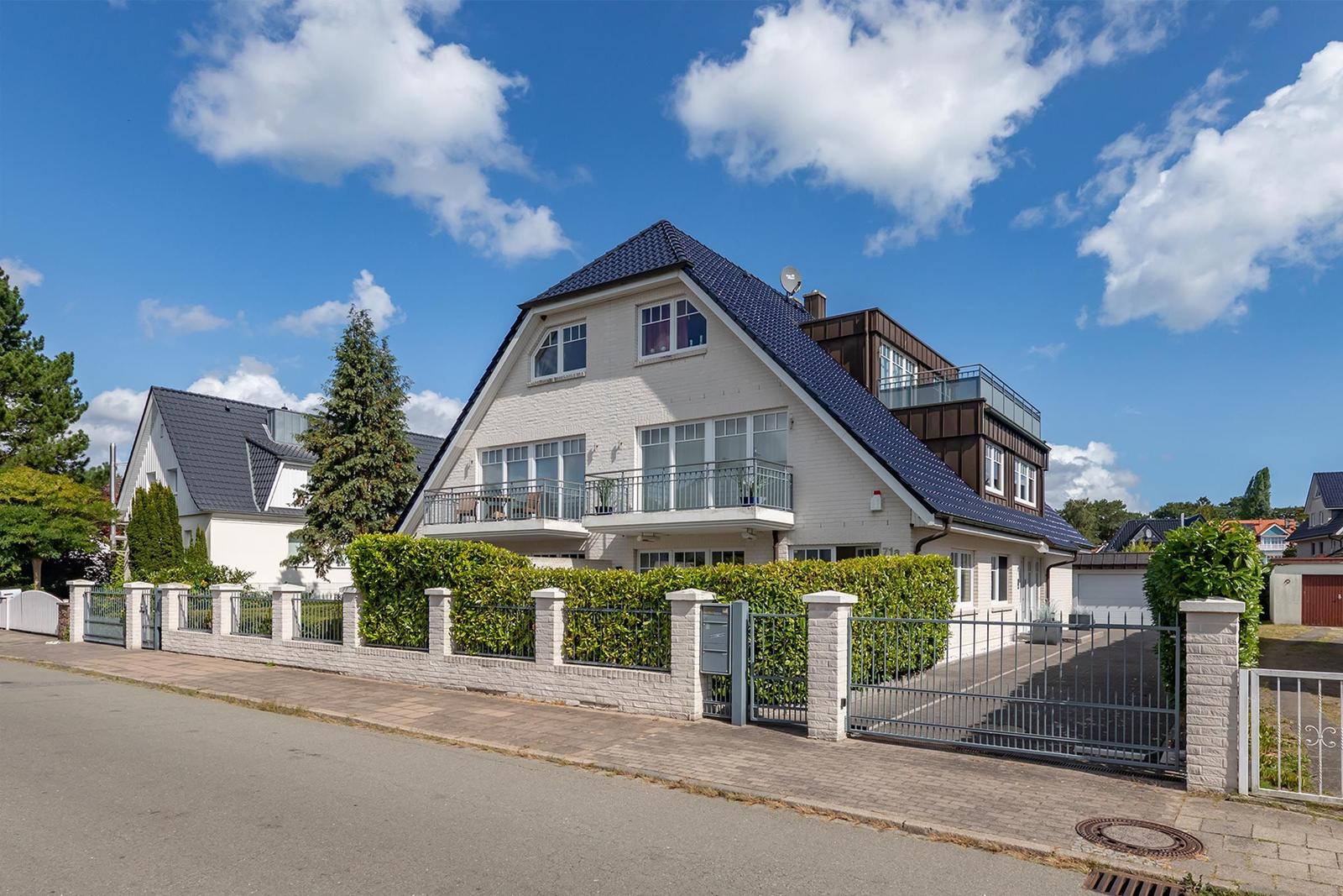 Modernes Haus mit Balkon und Gartenzaun unter blauem Himmel.