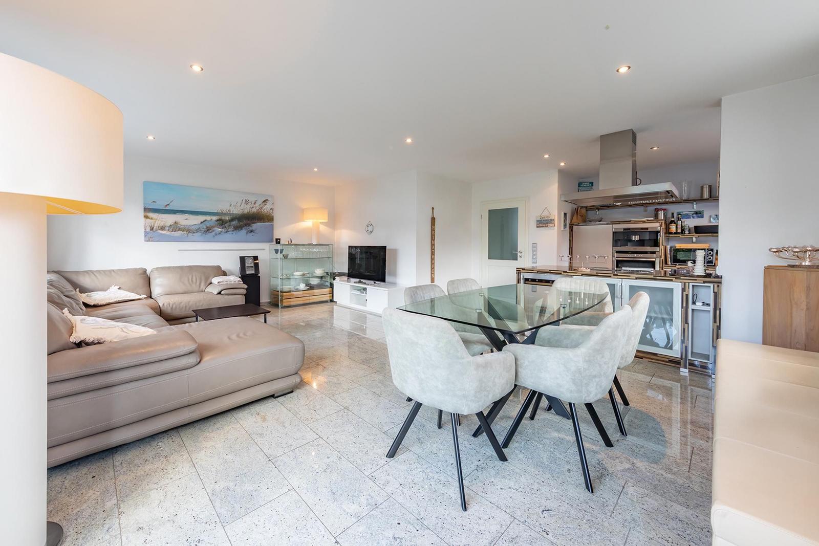 Wohn- und Essbereich mit Sofa, Glas-Tisch und moderner Küche.