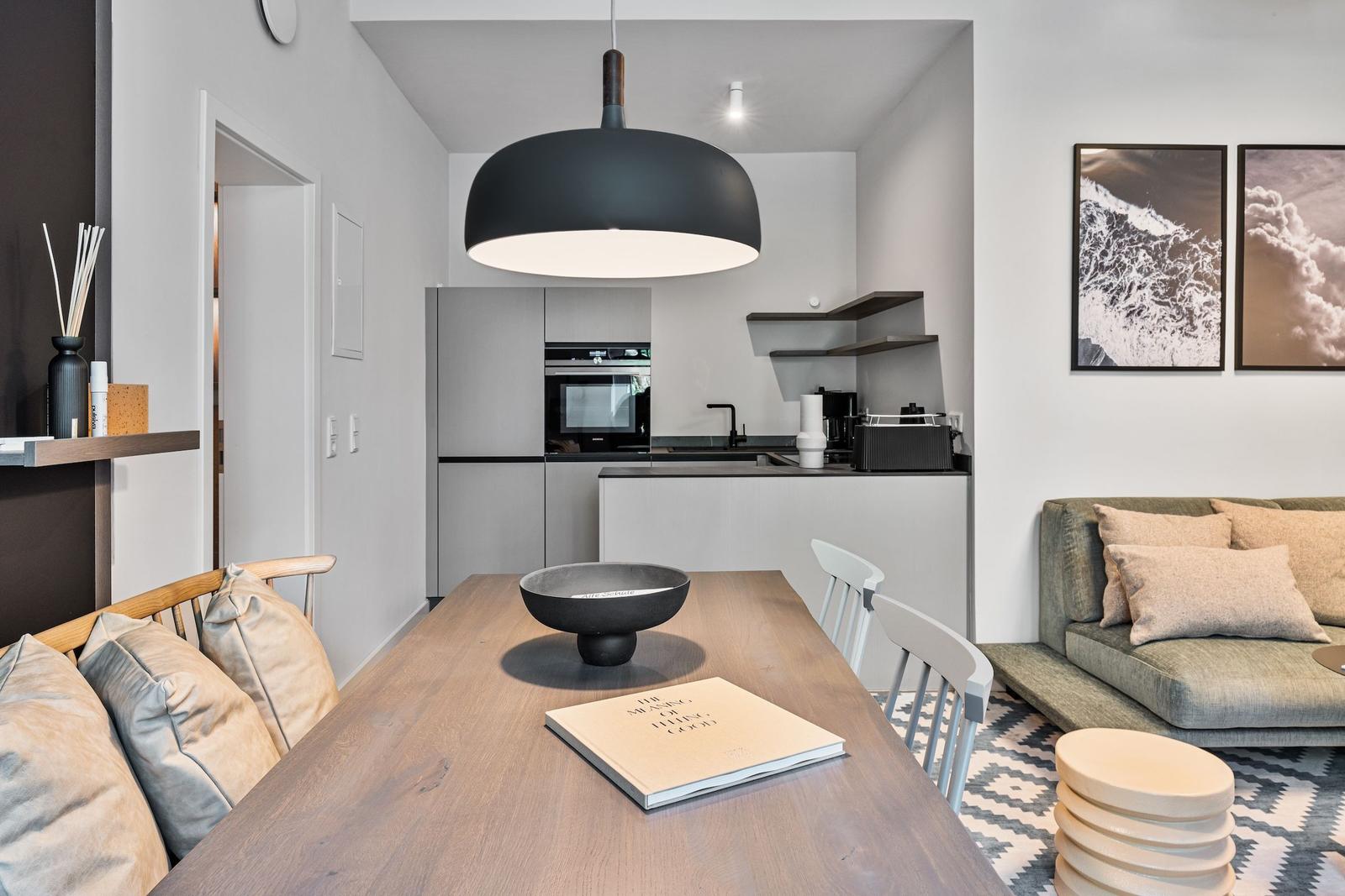 Dining area with table, chairs, and sofa. Kitchen with range hood and wall shelves.