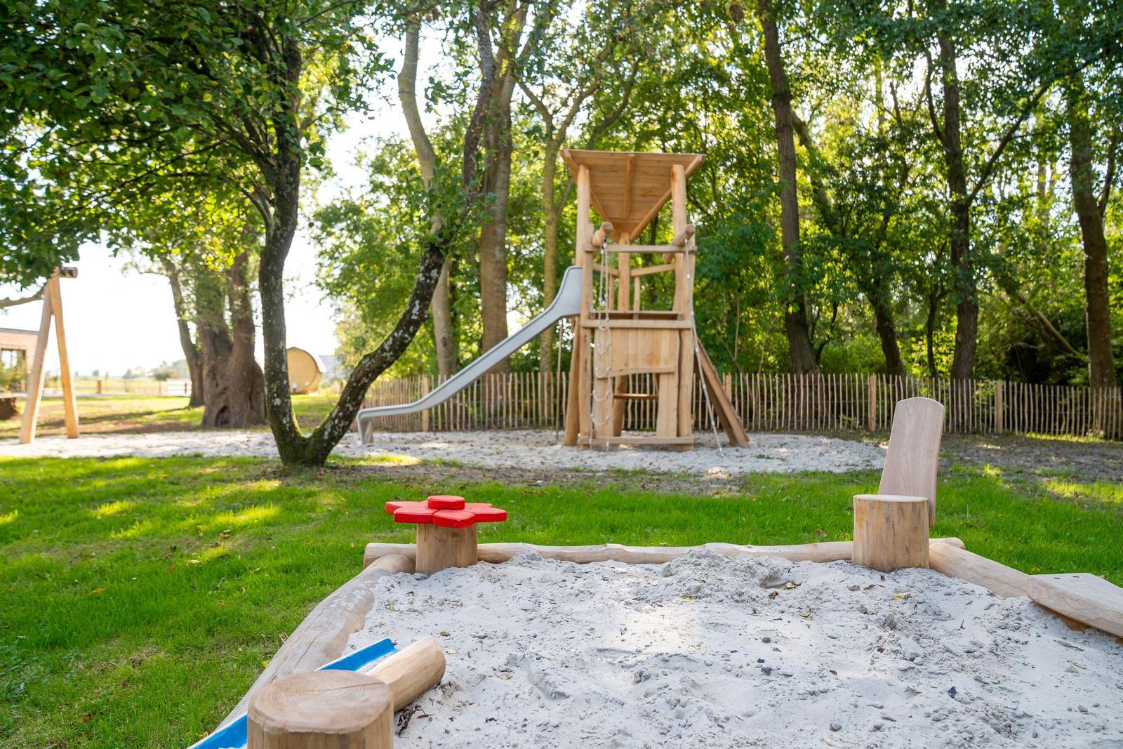 Playground with sandbox, slide, and wooden play equipment in greenery.
