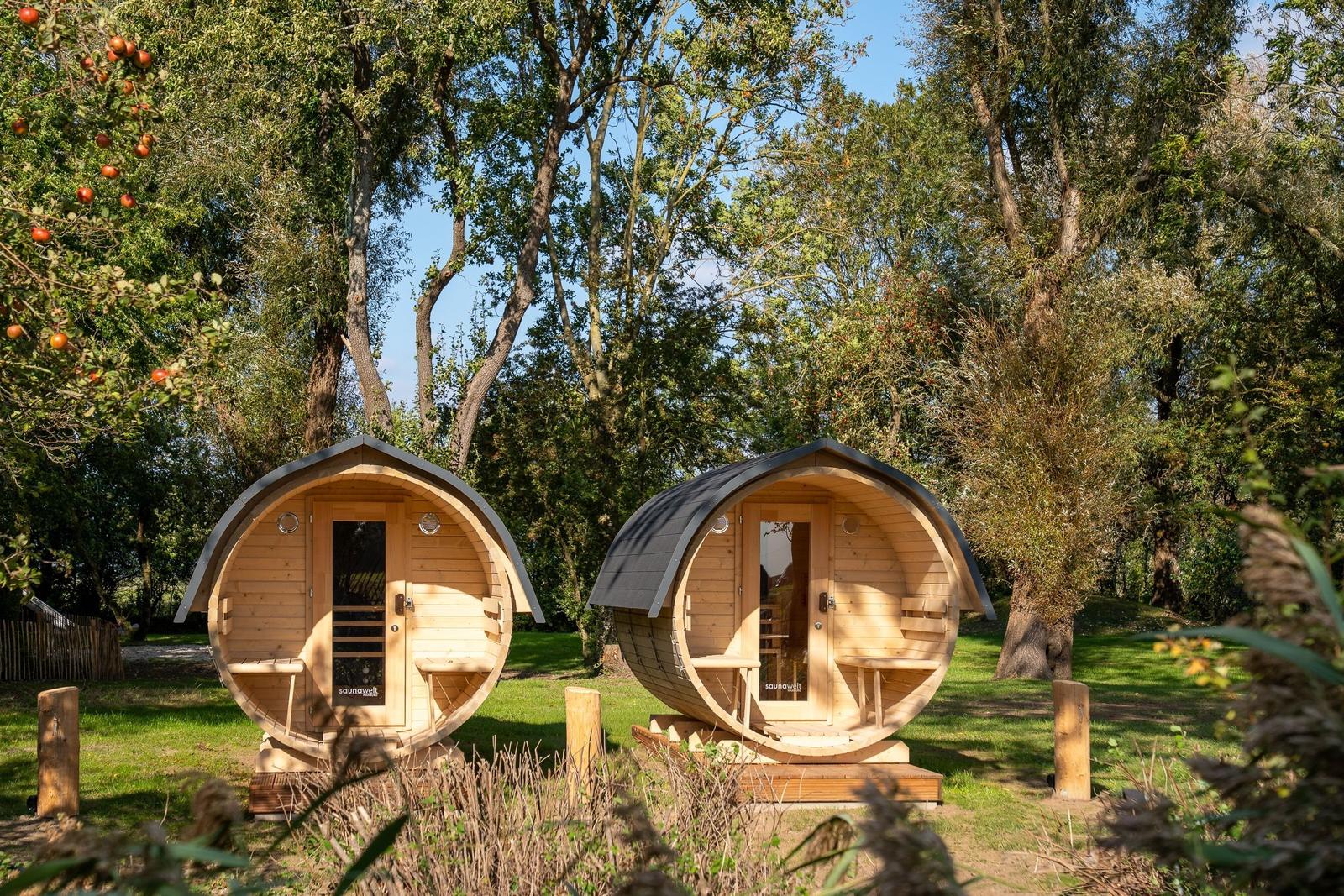 Two round wooden saunas stand in the green. Each has a door and benches.