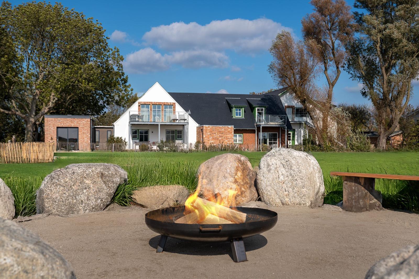 Fire pit in garden in front of house with large stones and trees.