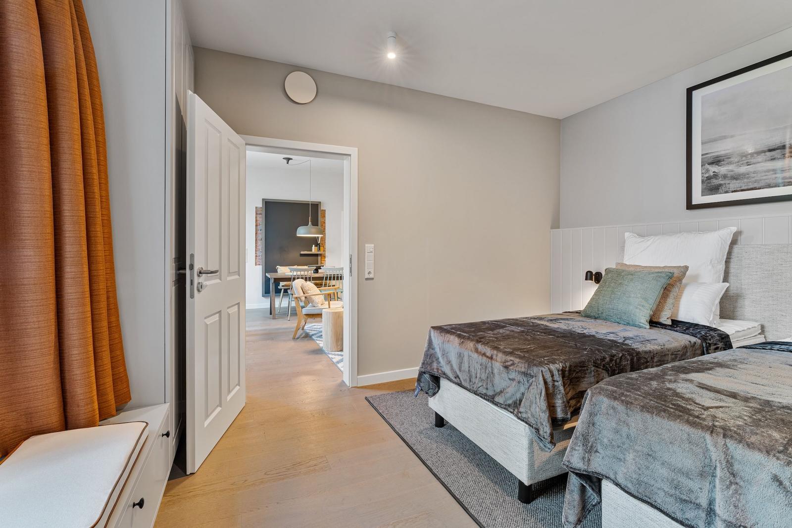 Two beds with blankets and pillows. Hallway to dining area with table and chairs.