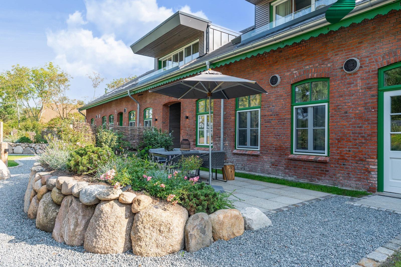 Red brick house with green trim, terrace, and garden with stone beds.