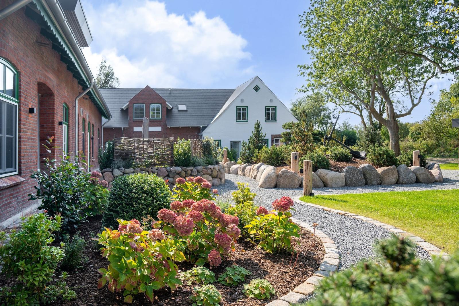 House with landscaped garden, stone path, and flower beds under blue sky.