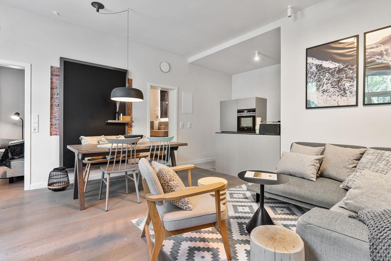 Living and dining area with sofa, table and chairs. Kitchen with refrigerator and oven.