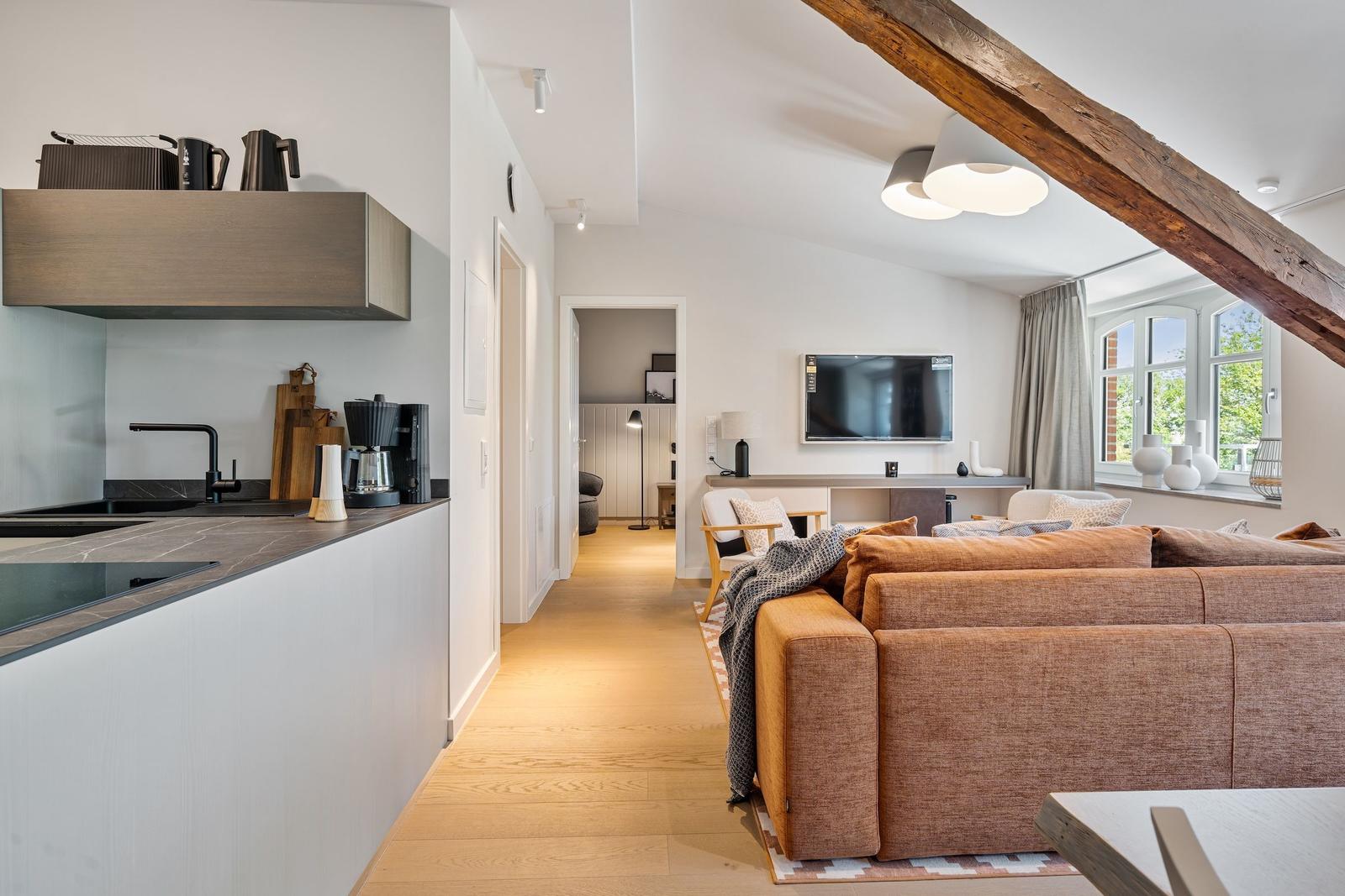 Apartment with kitchen, living area, and wooden beam. Sofa, TV, and window visible.