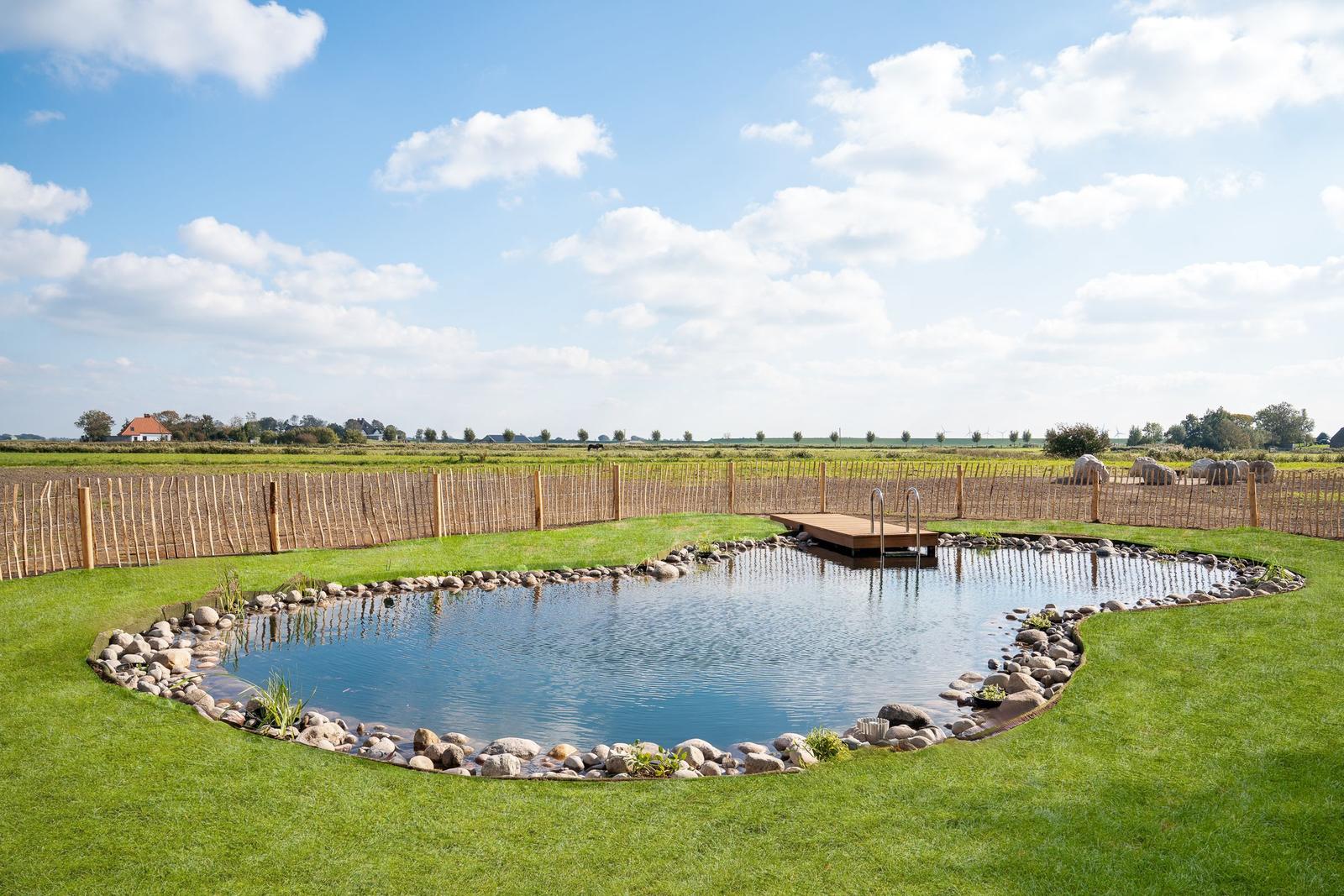 A large oval pool with stone edge and wooden platform in the green garden.