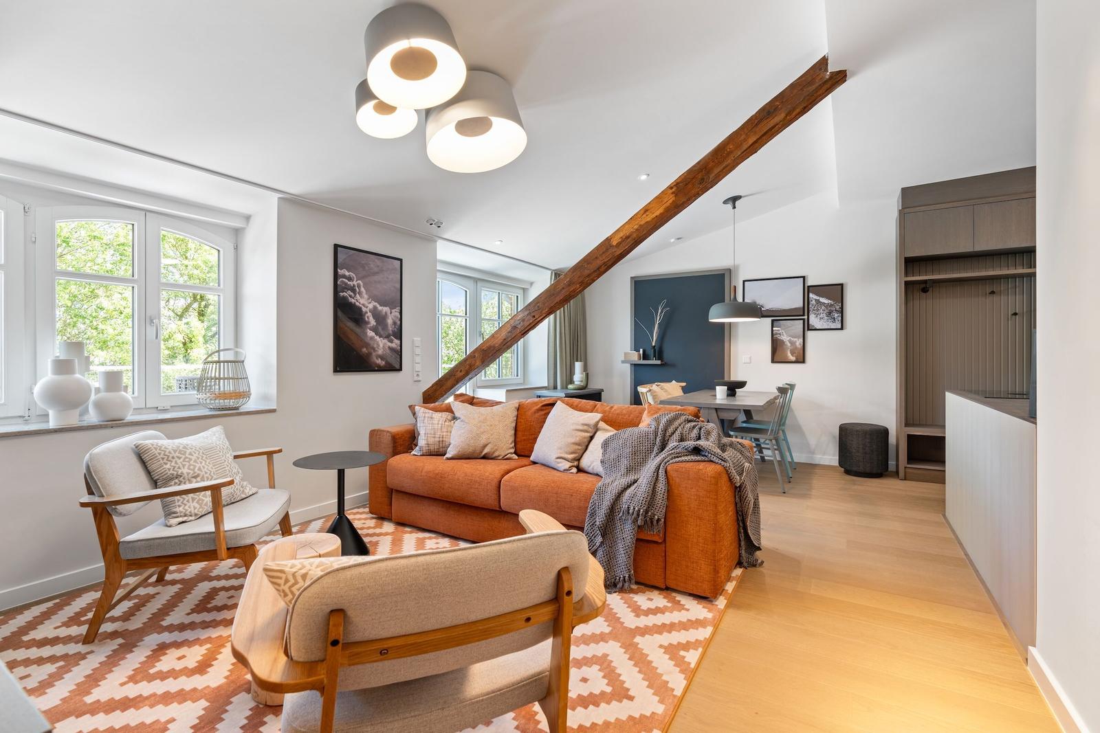 Living area with sofa, chairs, and wooden beam. Dining area with table and chairs.