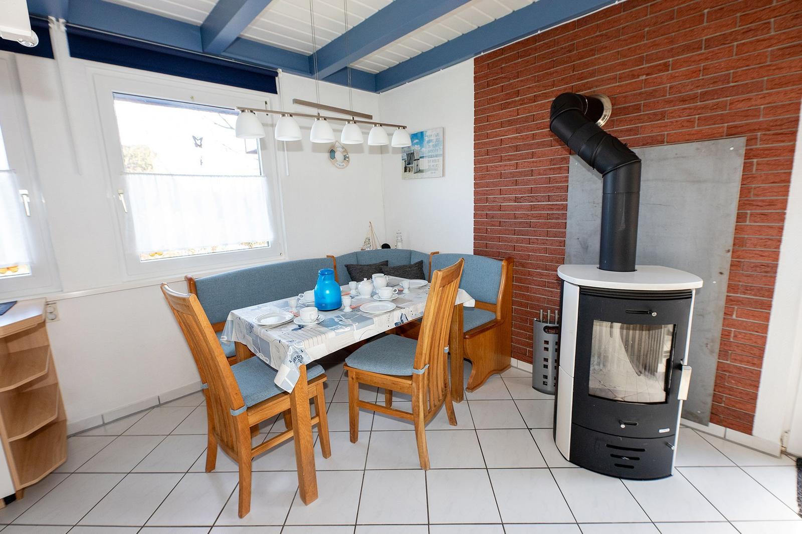 Esszimmer mit Sitzbank, Holzstühlen und Kaminofen an Backsteinwand.