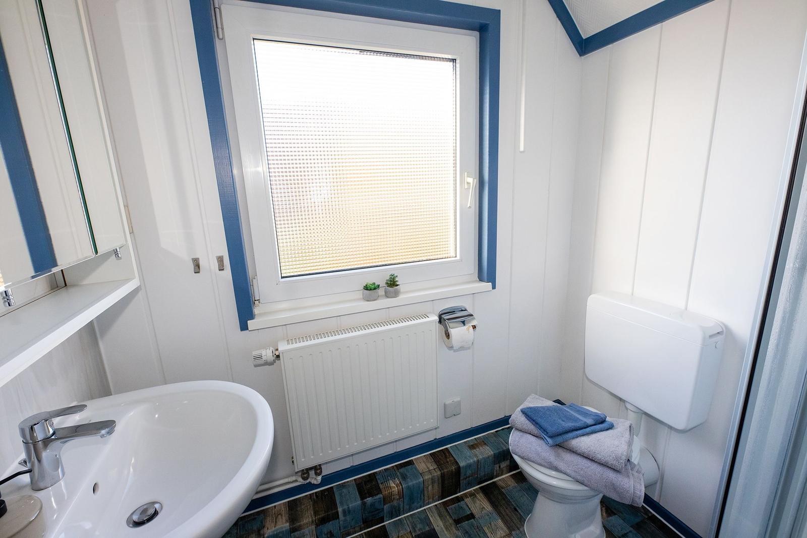 Badezimmer mit Waschbecken, Toilette und Fenster mit Jalousie.