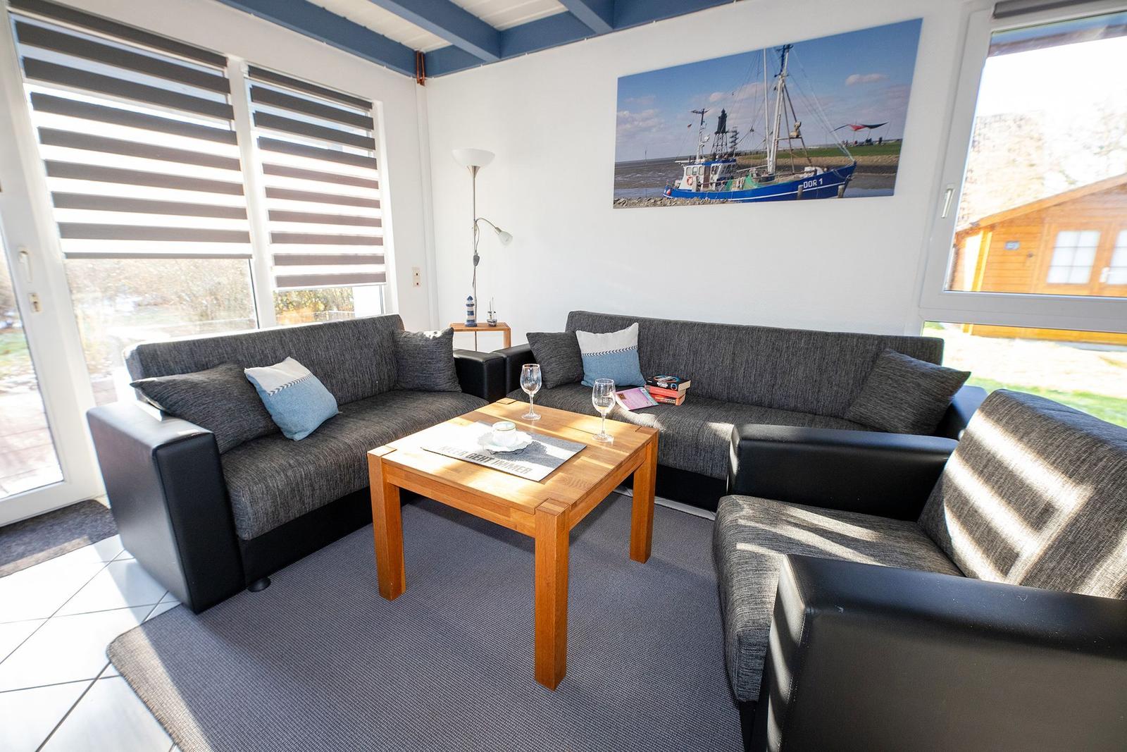 Wohnzimmer mit Sofa, Sessel und Tisch. Wandbild zeigt Fischerboot.