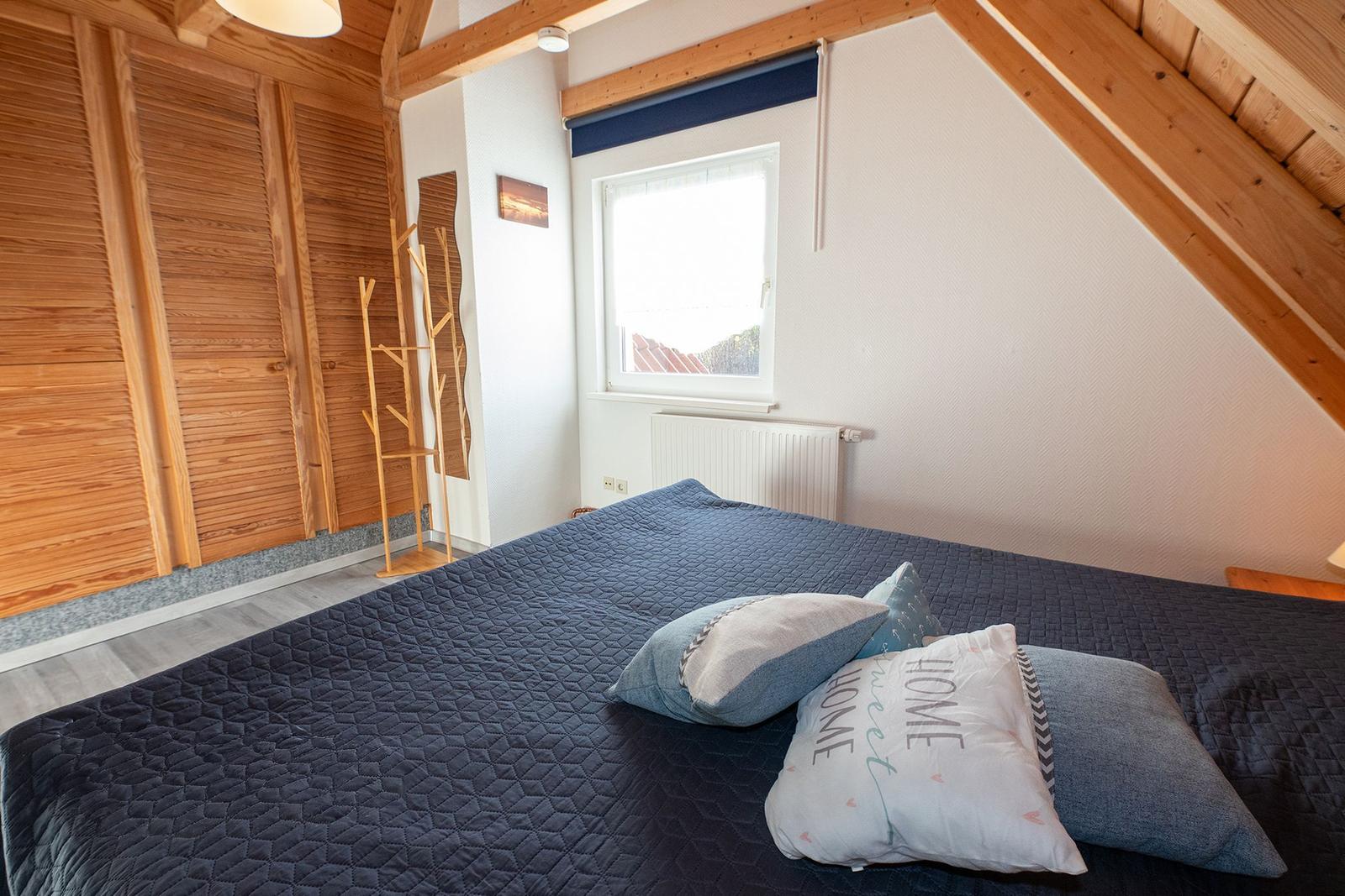 Schlafzimmer mit Dachschrägen, Bett, Kleiderständer und Fenster.