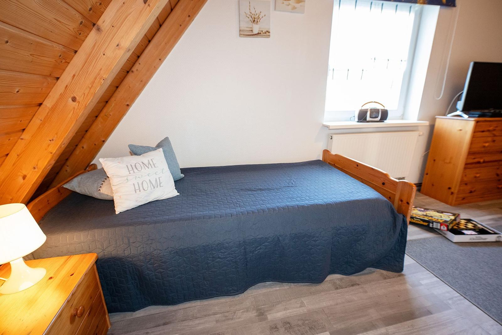 Schlafzimmer mit Dachschrägen, Bett, Nachttisch, Fernseher und Fenster.