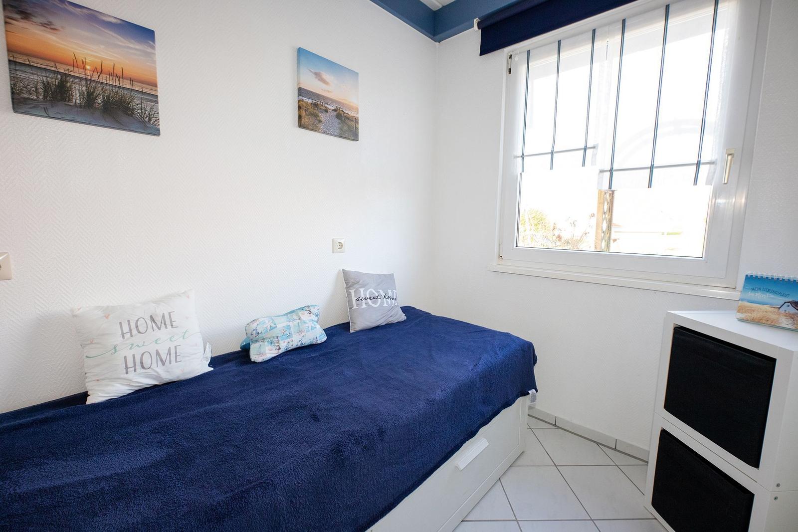 Ein Schlafzimmer mit blauer Bettdecke, Fenster und Wandbildern.