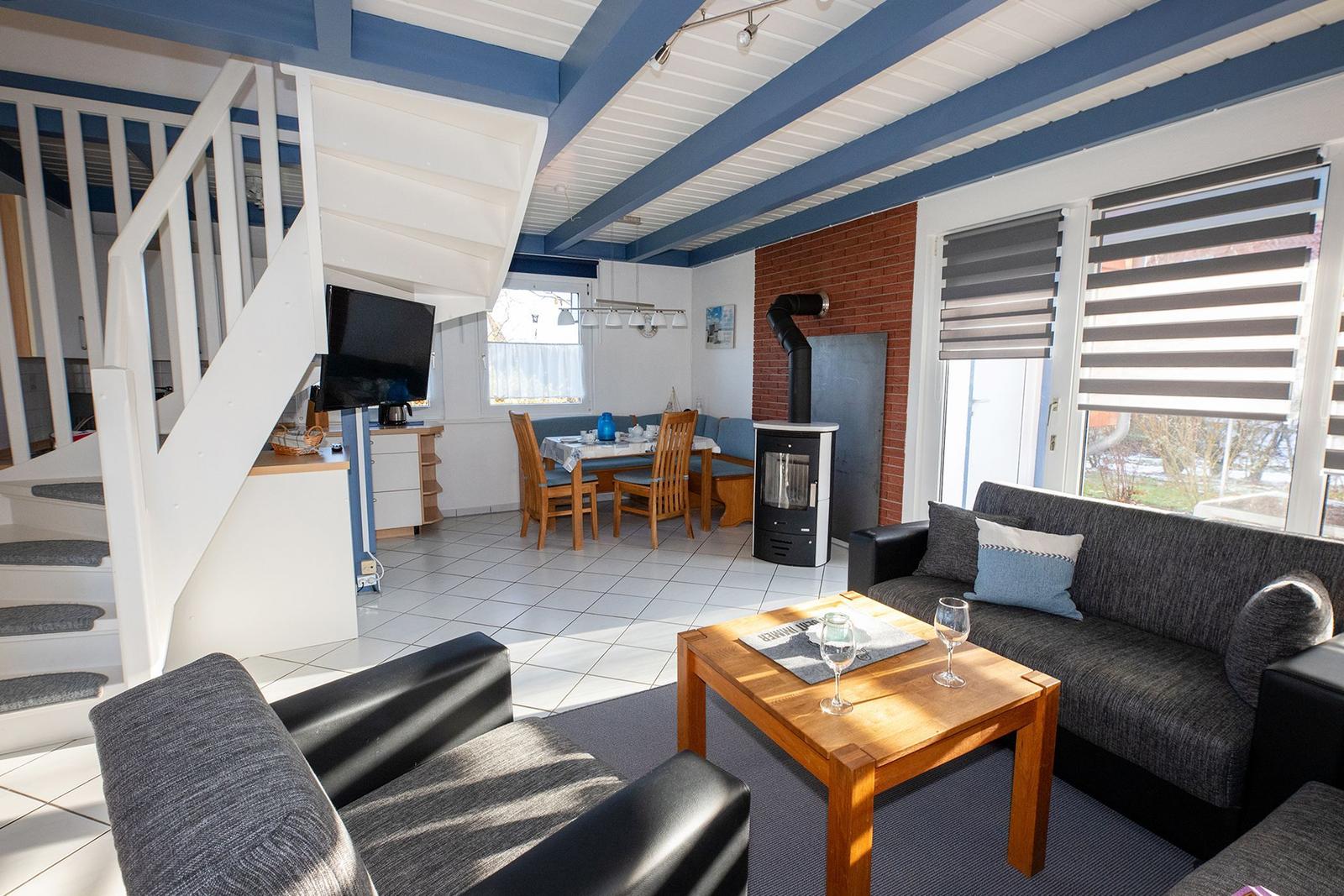 Wohn- und Essbereich mit Holztisch, Sofa und Kaminofen. Treppe führt zur Küche.