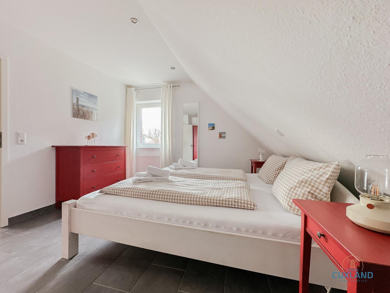 Schlafzimmer mit Doppelbett, rotem Schrank und Fenster.