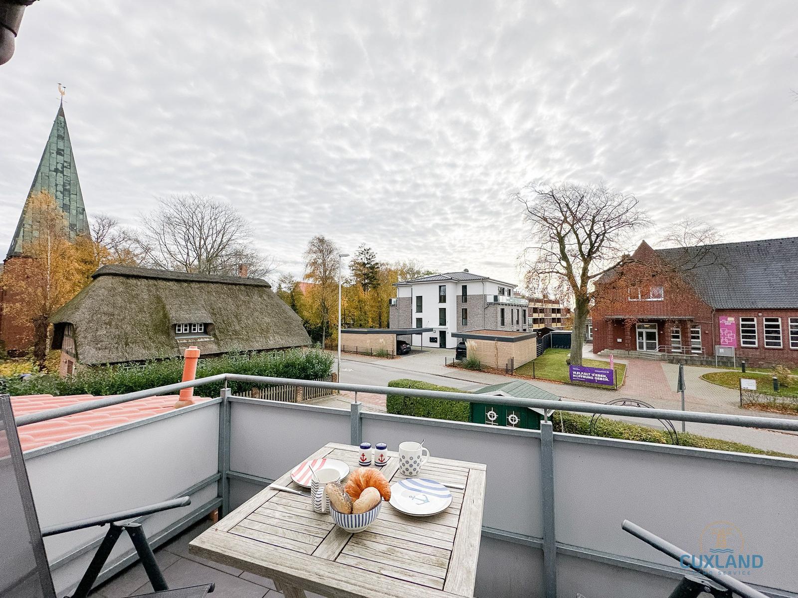 Terrasse mit Tisch und Stühlen. Blick auf Dorf mit Kirche und traditionellem Haus.