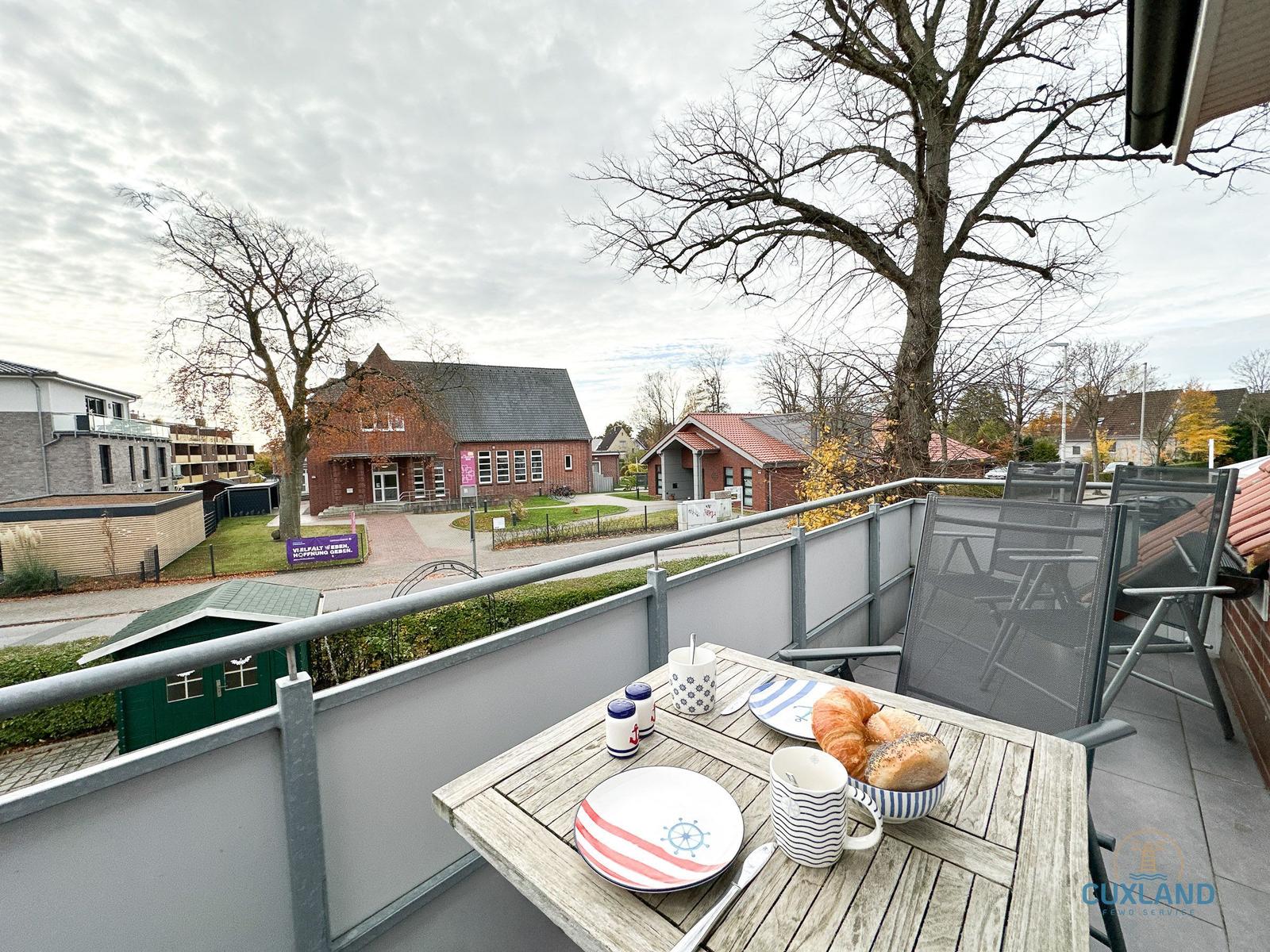 Terrasse mit Tisch, Stühlen und Frühstück. Blick auf Gebäude und Bäume.