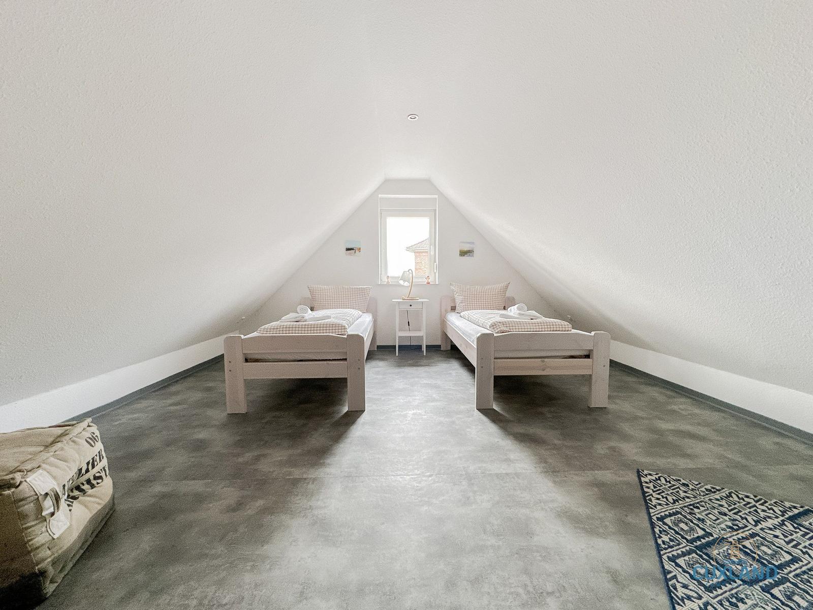 Zwei Einzelbetten stehen unter einem Dachbodenfenster mit einem Nachttisch dazwischen.