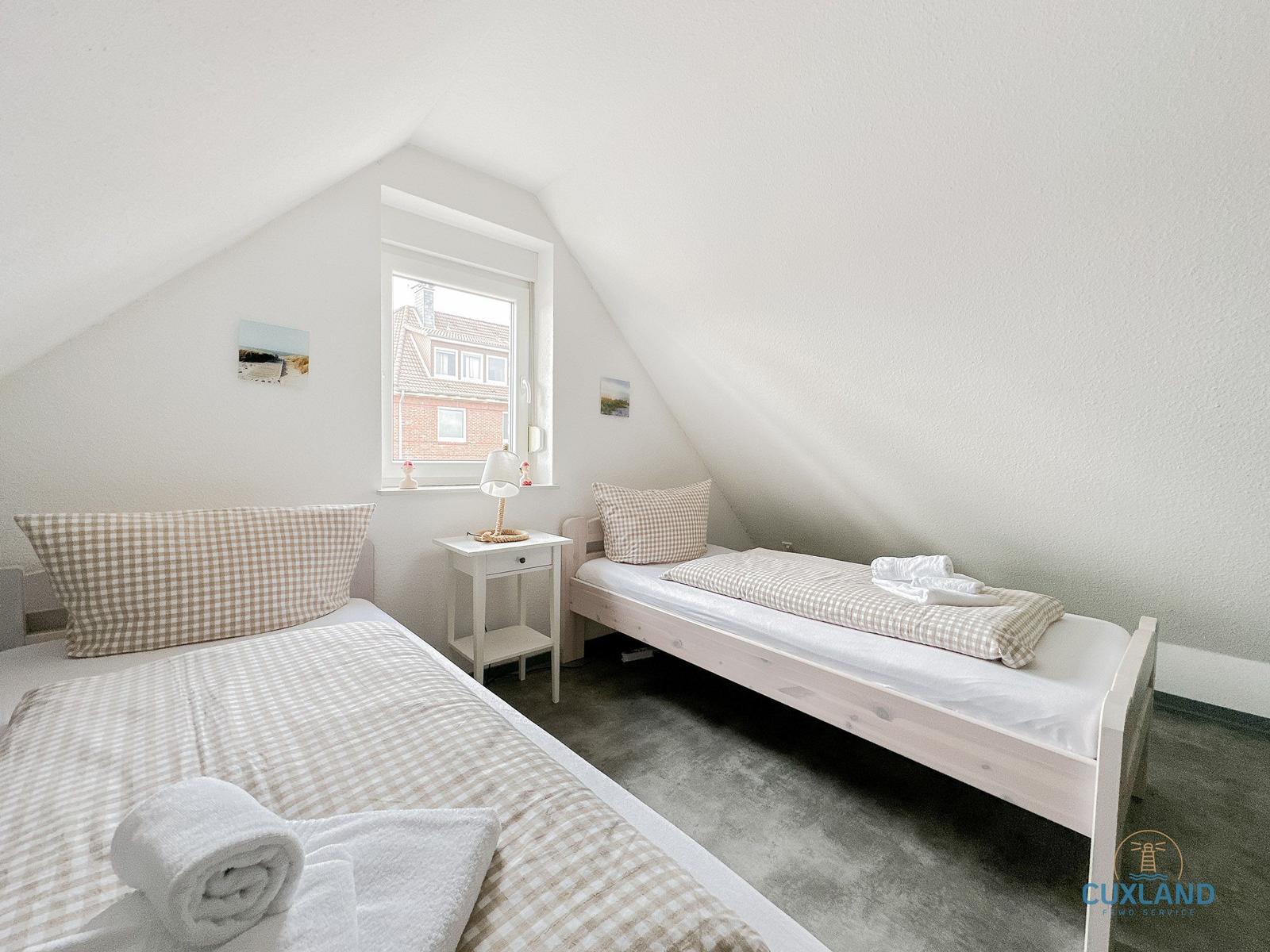 Zwei Betten mit Bettwäsche und ein Fenster in einem Dachzimmer.