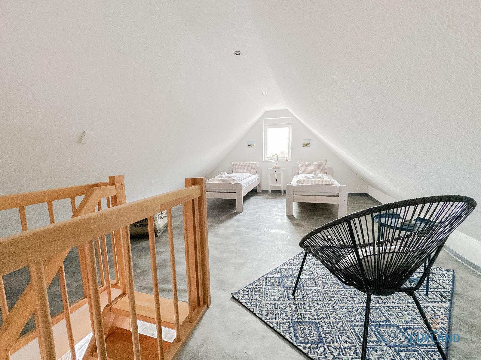 Zimmer mit zwei Betten, Treppe und Sitzgelegenheit im Dachgeschoss.