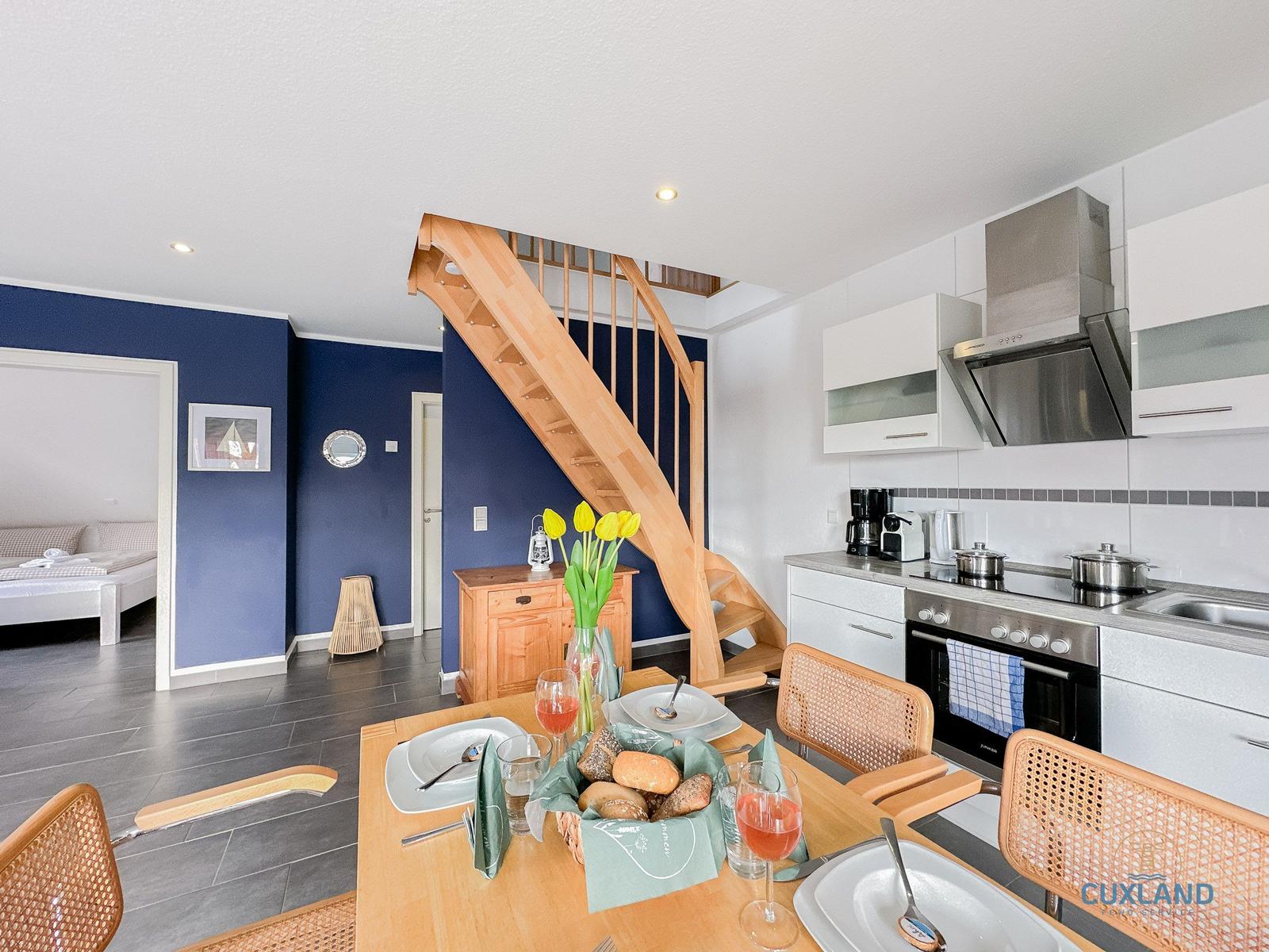 Küche mit Esstisch, Holztreppe und Schlafzimmer im Hintergrund.