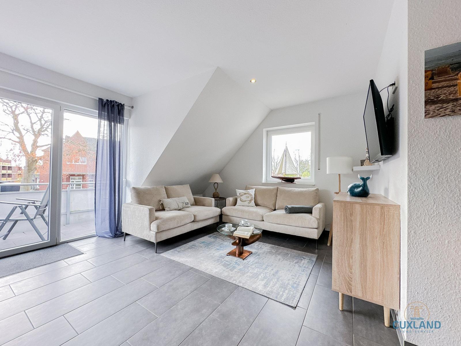 Wohnzimmer mit zwei Sofas, Glas-Tisch und TV. Balkon über Schiebetür. Dachgeschoss mit Dachschrägen.