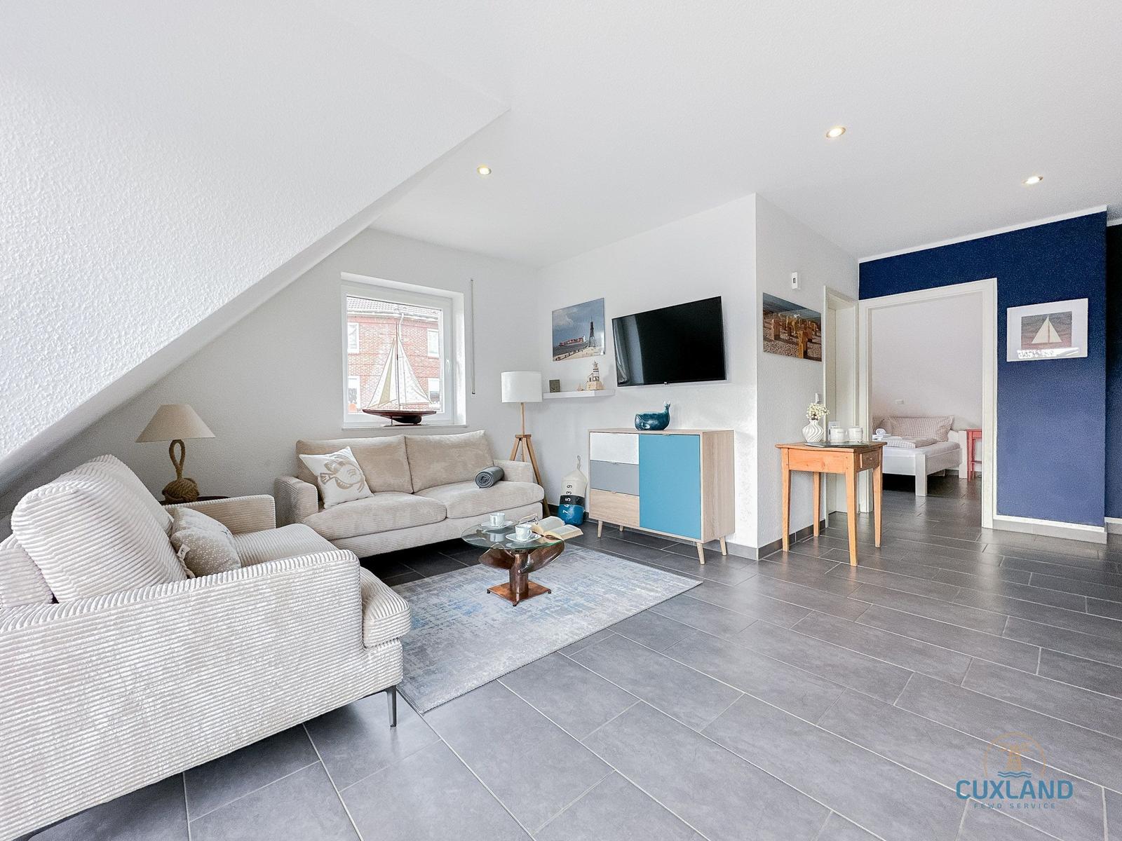 Wohnzimmer mit Sofa, Fernseher und Blick auf Schlafzimmer.