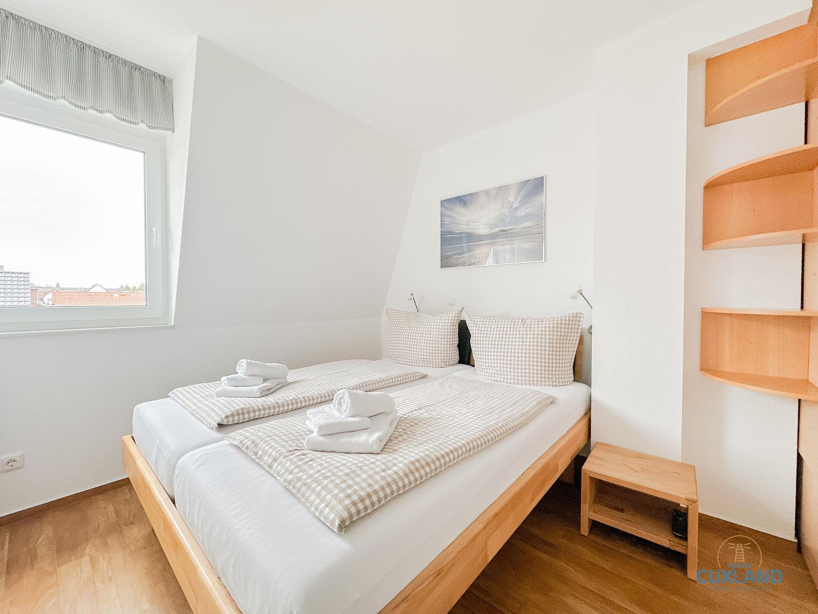 Schlafzimmer mit Doppelbett, Fenster und Holzregal.