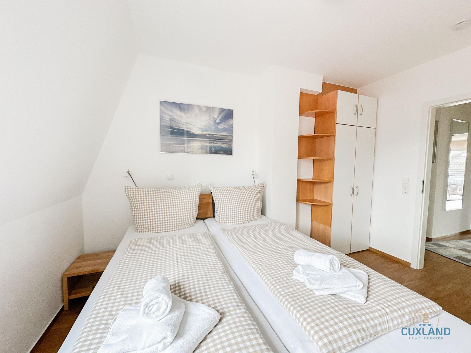 Zwei Betten mit Kissen und Handtüchern. Holzregal und Wandbild.