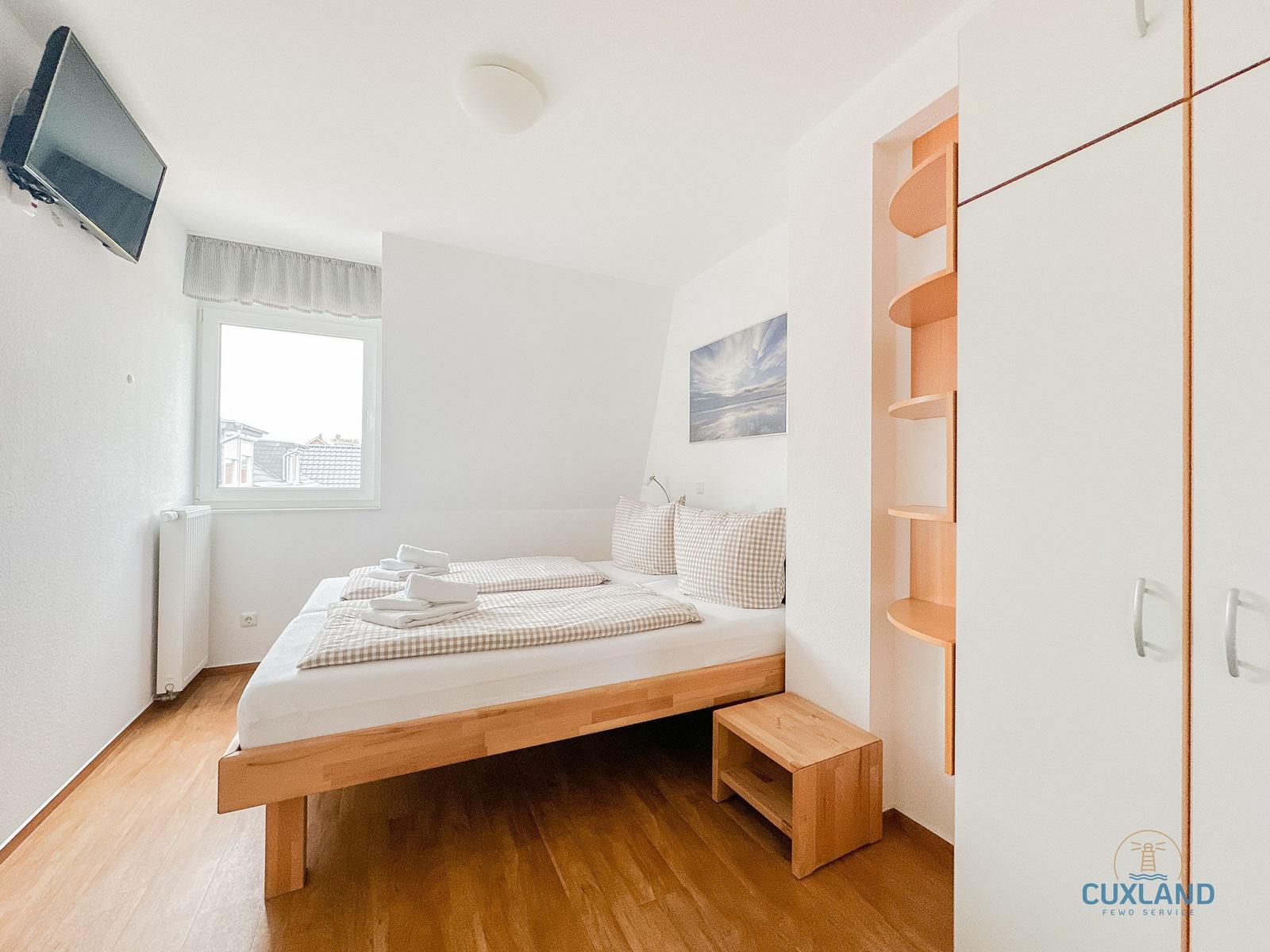 Schlafzimmer mit Bett, TV, Fenster und Kleiderschrank.