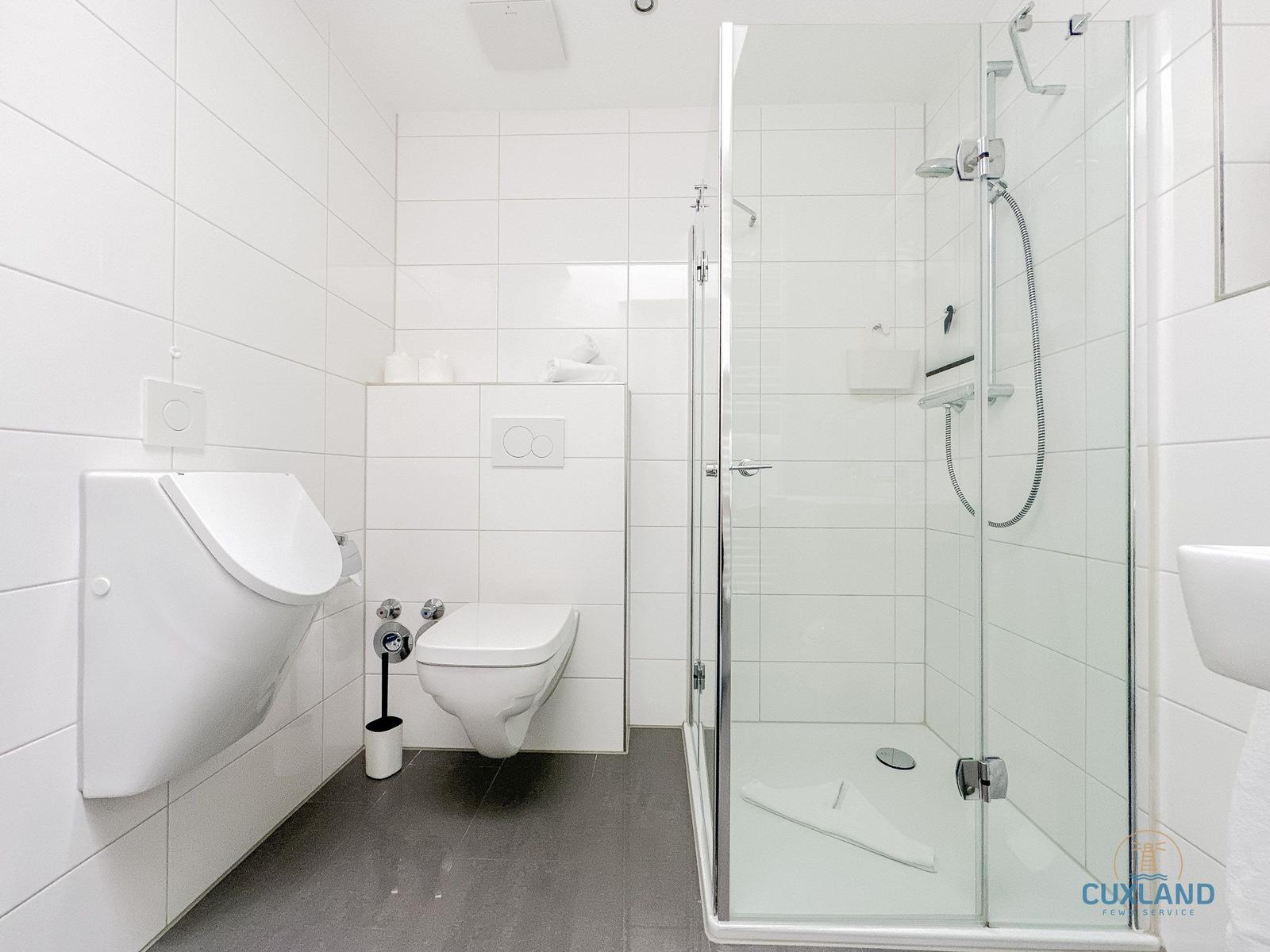 Badezimmer mit Dusche, WC und Bidet. Fliesen und grauer Boden.
